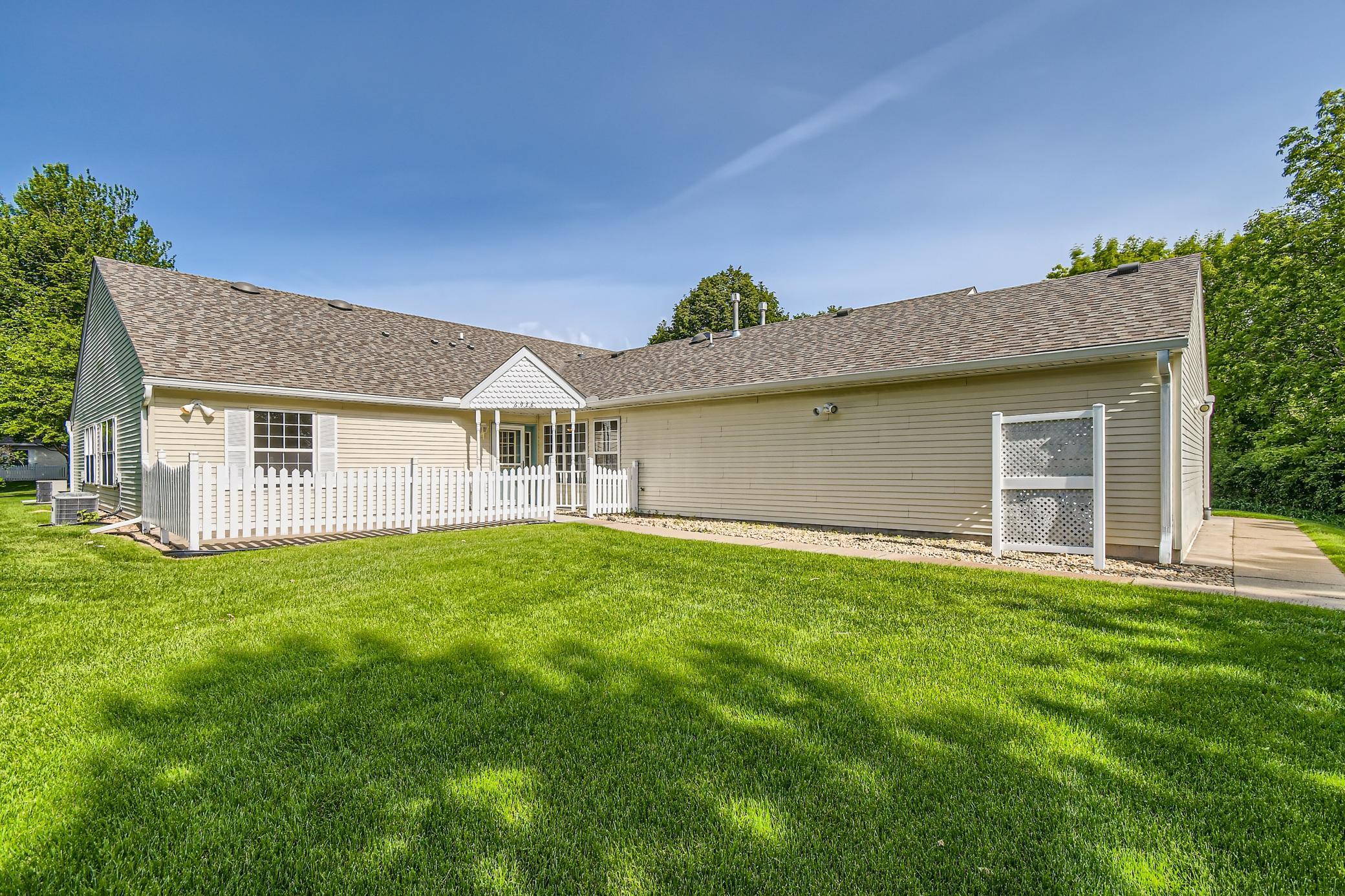 Rear of a beige-sided home with a white fenced patio and broad green lawn.