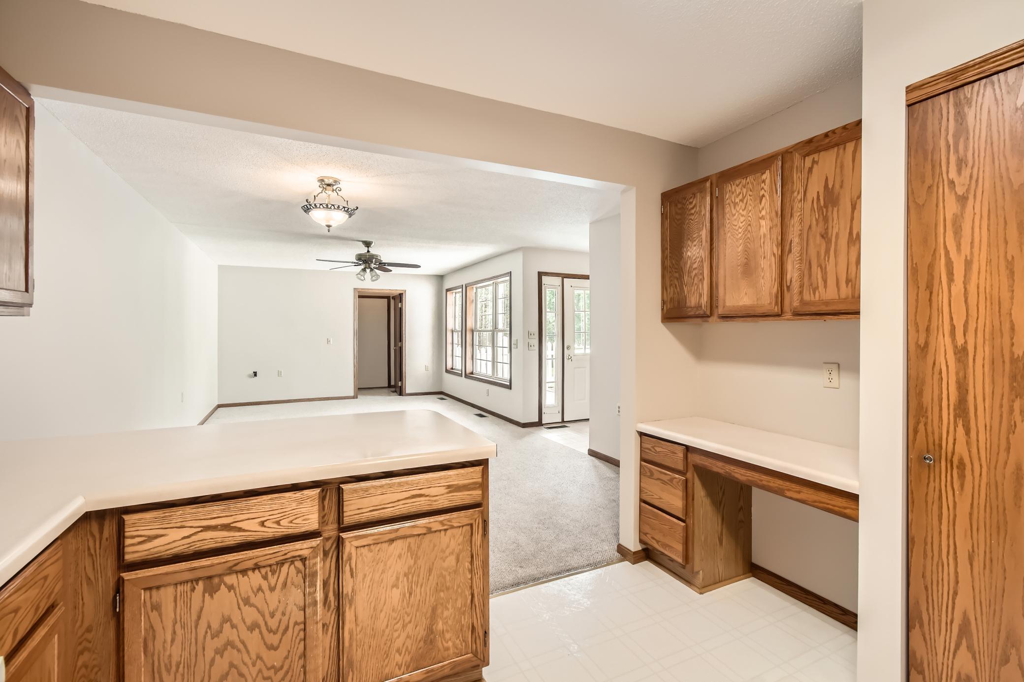 Kitchen with oak cabinets and white countertops opening to a carpeted living area and patio door.