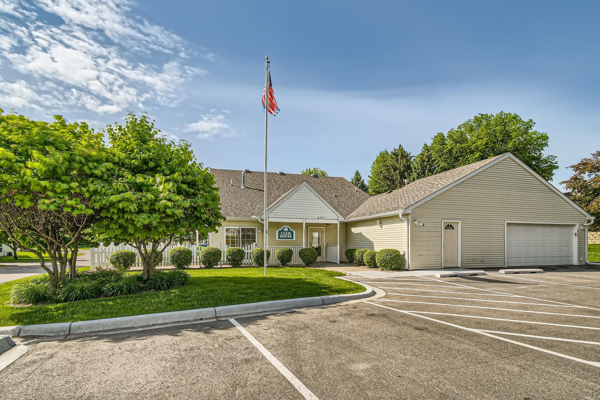 Community clubhouse with a two-car garage, white fence, and American flag.