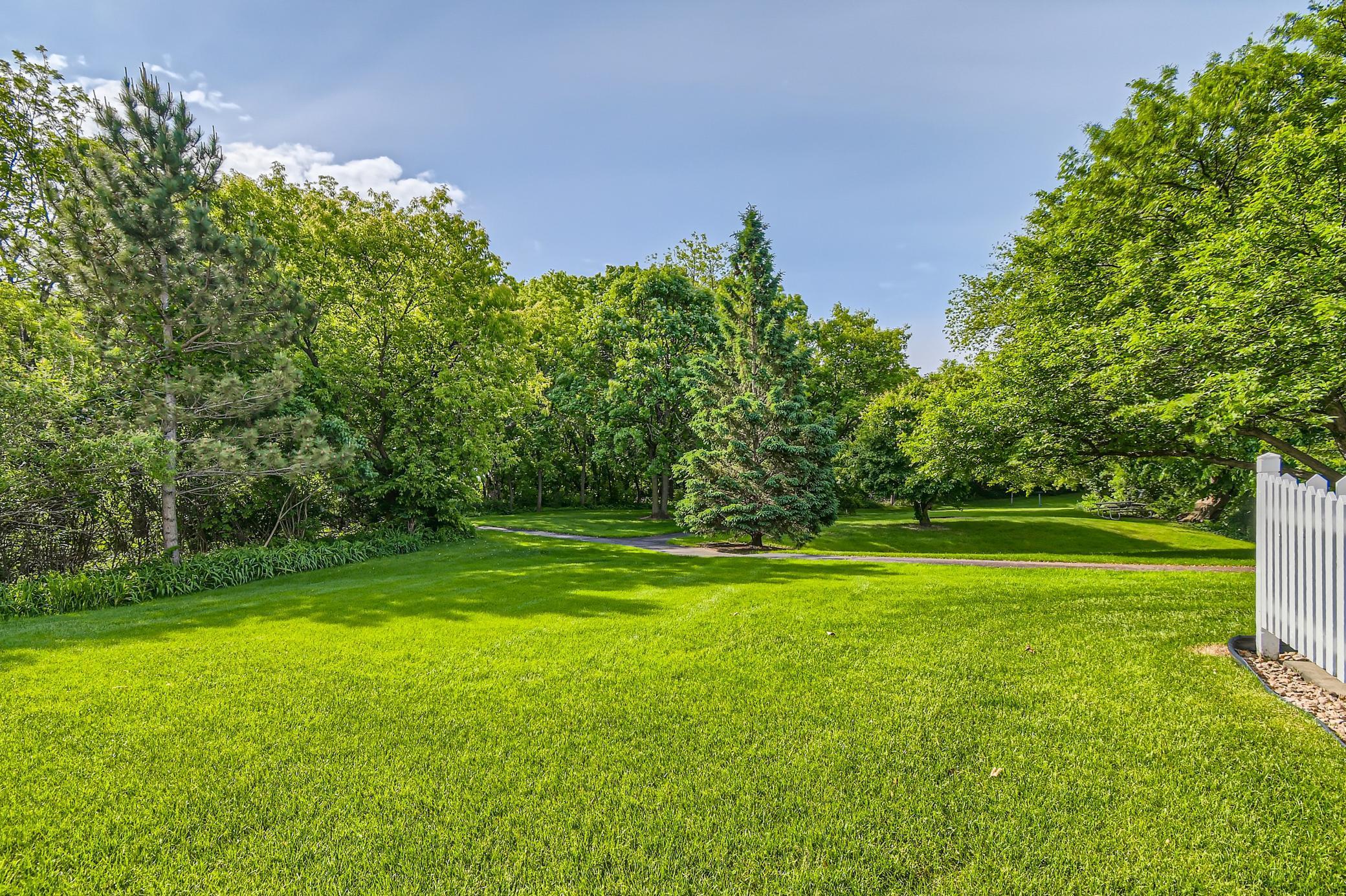 Landscaped lawn with mature trees, a curving path, and a white picket fence.