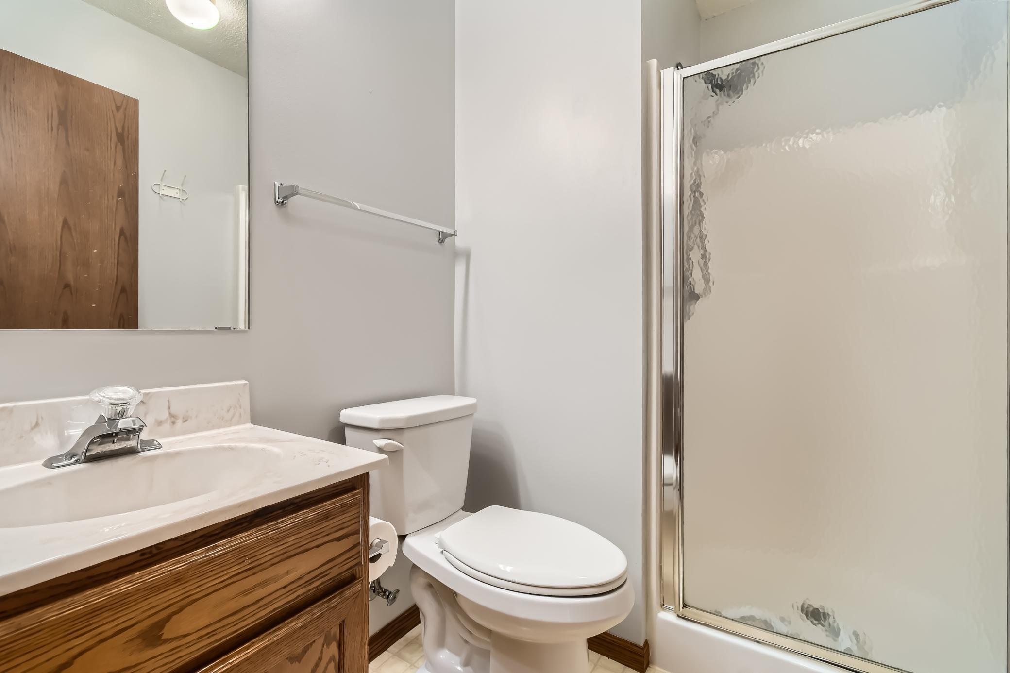 Bathroom with a wood-grain vanity, white toilet, and frosted-glass shower enclosure.
