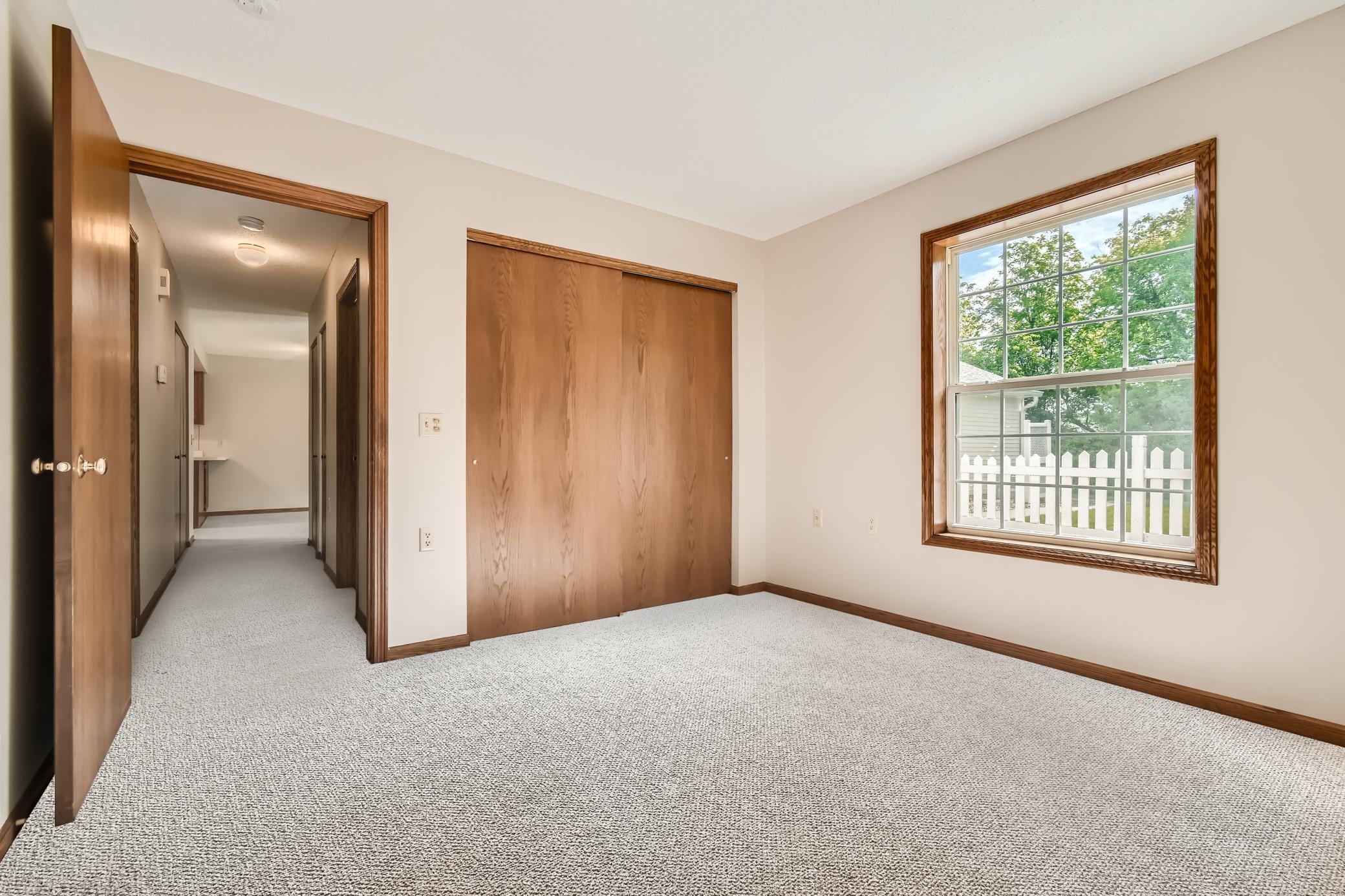 Empty bedroom with a large wood sliding-door closet and a window overlooking a white picket fence.