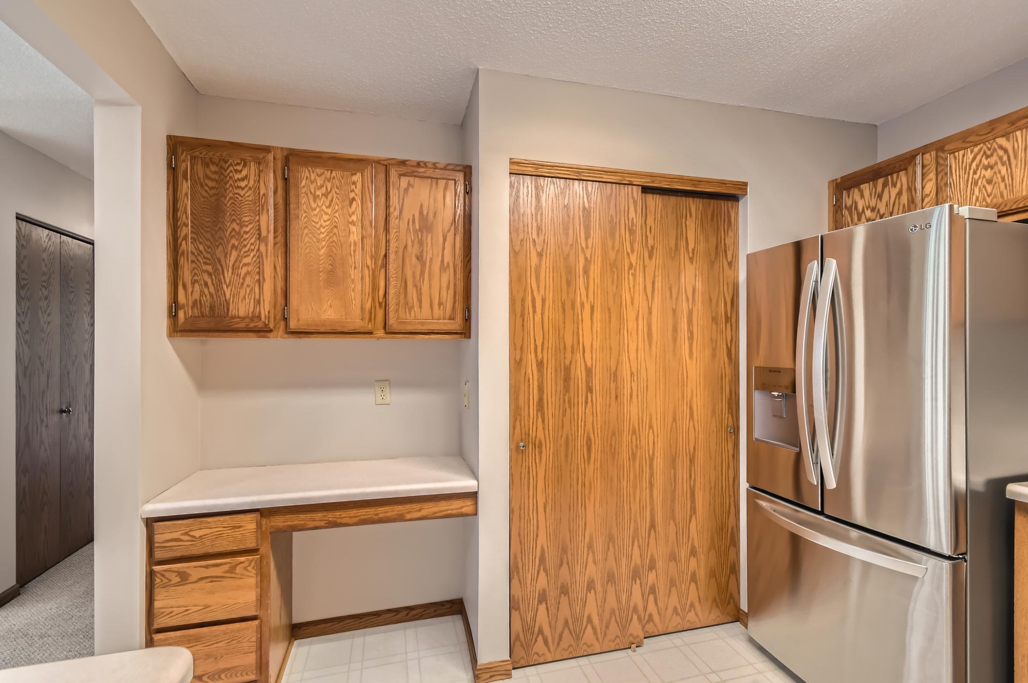 Kitchen with oak cabinetry, a built-in desk, sliding wood door, and stainless steel refrigerator.