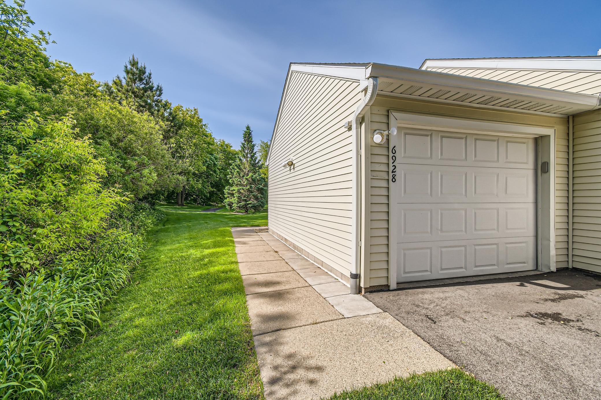 Attached white garage beside a concrete walkway, green lawn, and mature trees.