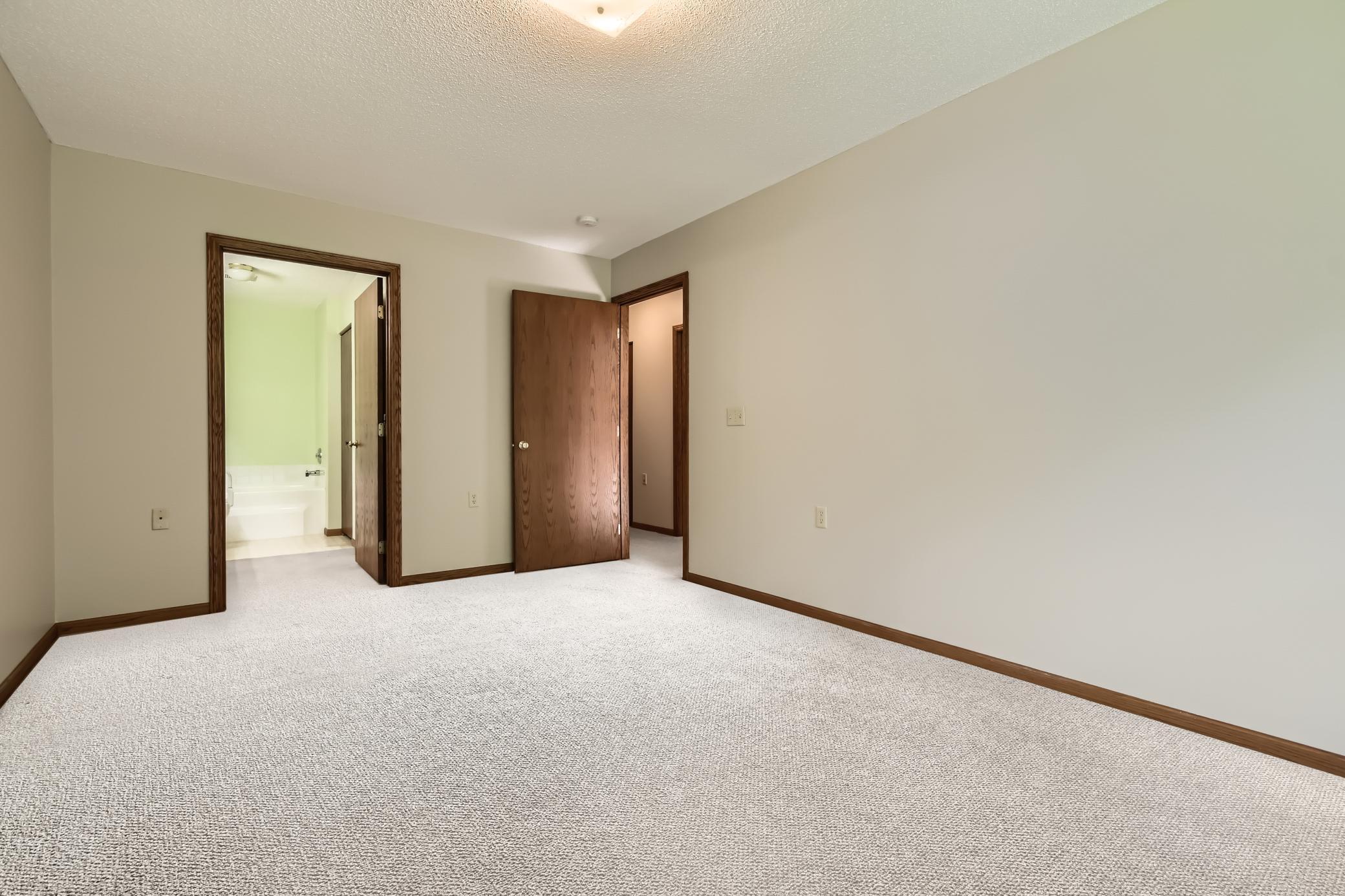 Empty bedroom with wall-to-wall carpet and open doorways to a bathroom and hallway.