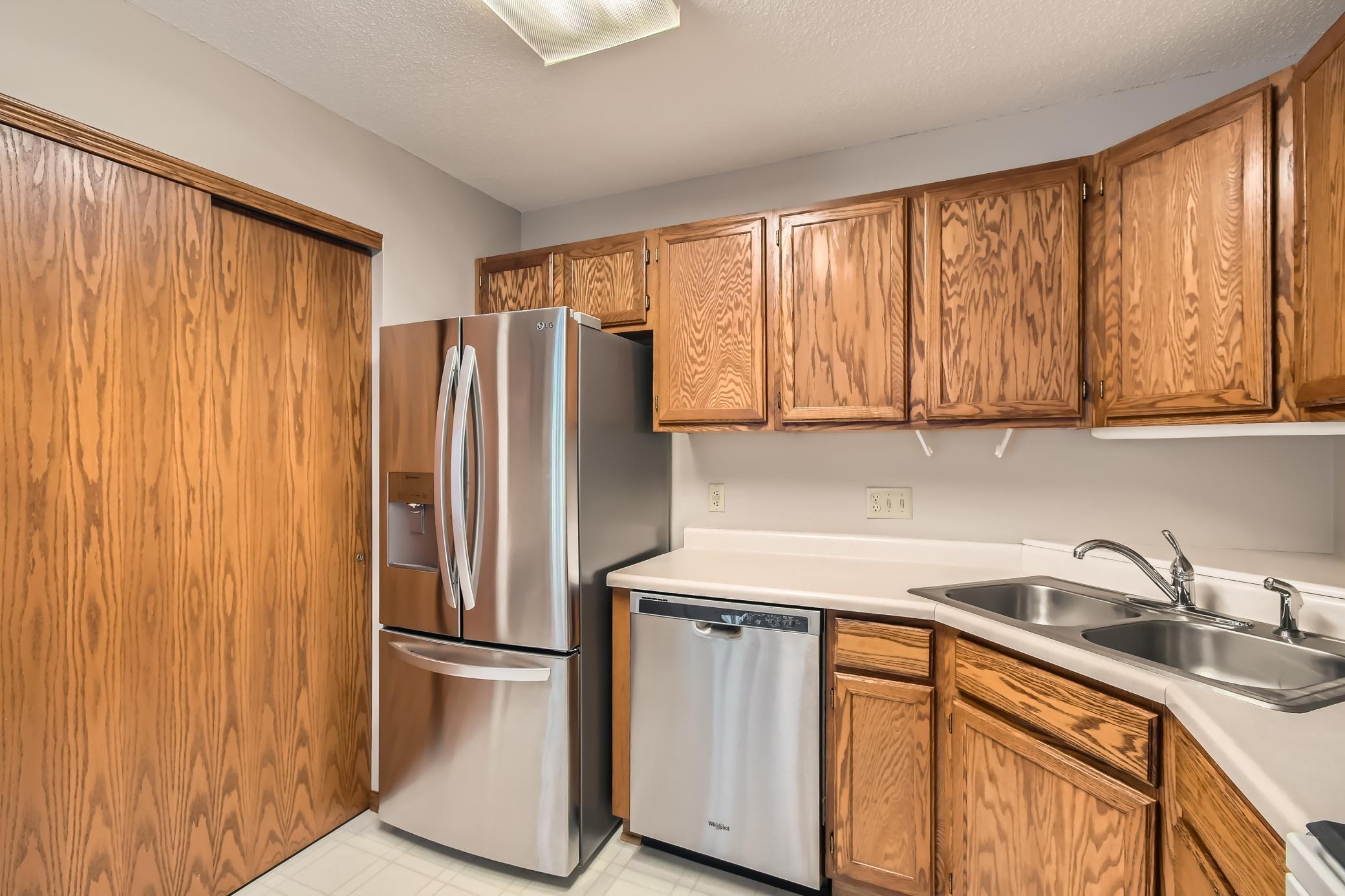 Kitchen with oak cabinets, stainless steel refrigerator and dishwasher, and a double-basin sink.