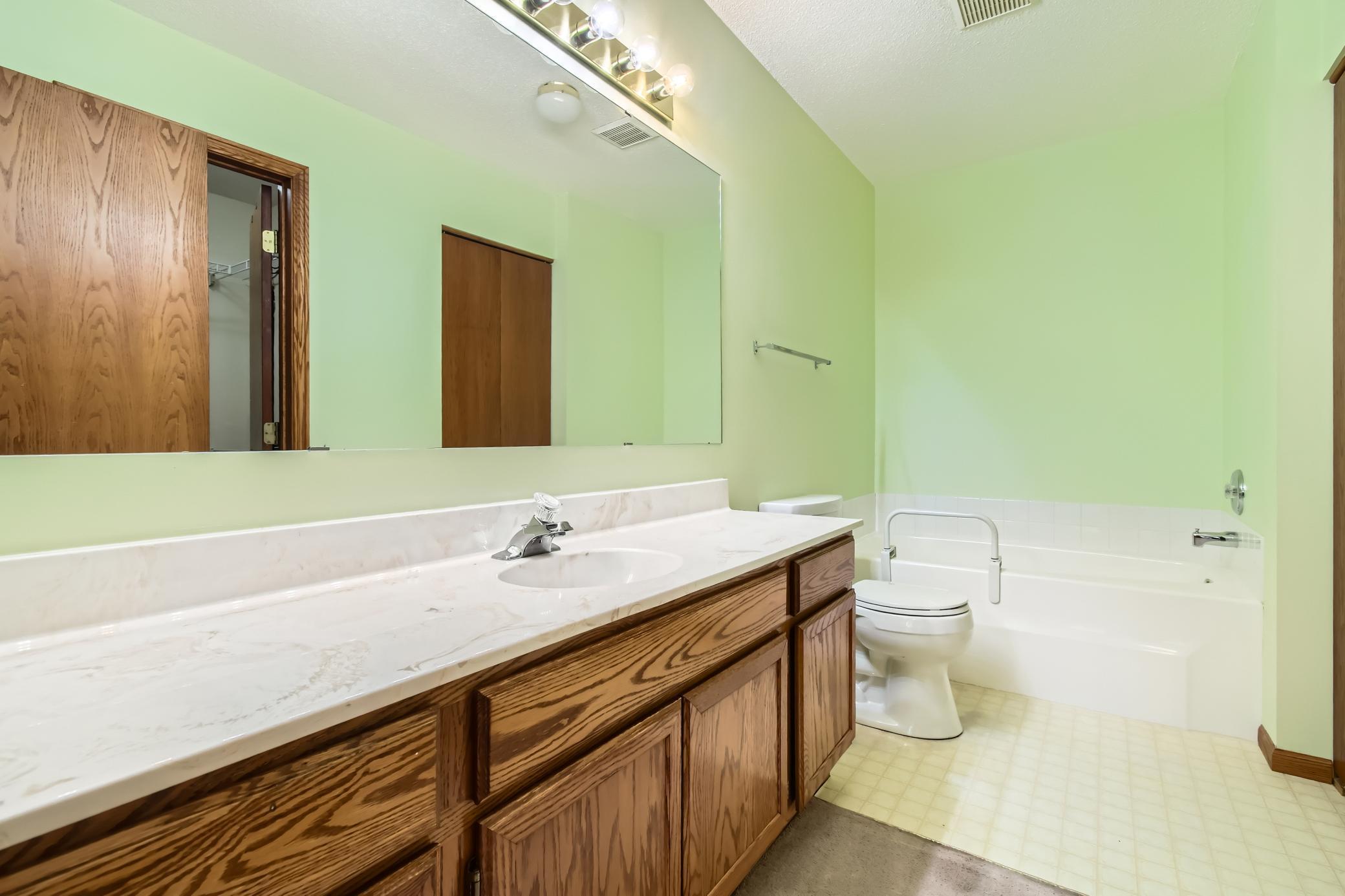 Bathroom with a long oak vanity, large mirror, and bathtub beside the toilet.