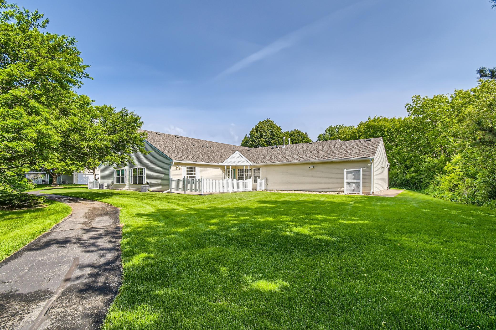 Rear of a beige-sided home with a white fenced patio, broad lawn, and mature trees.