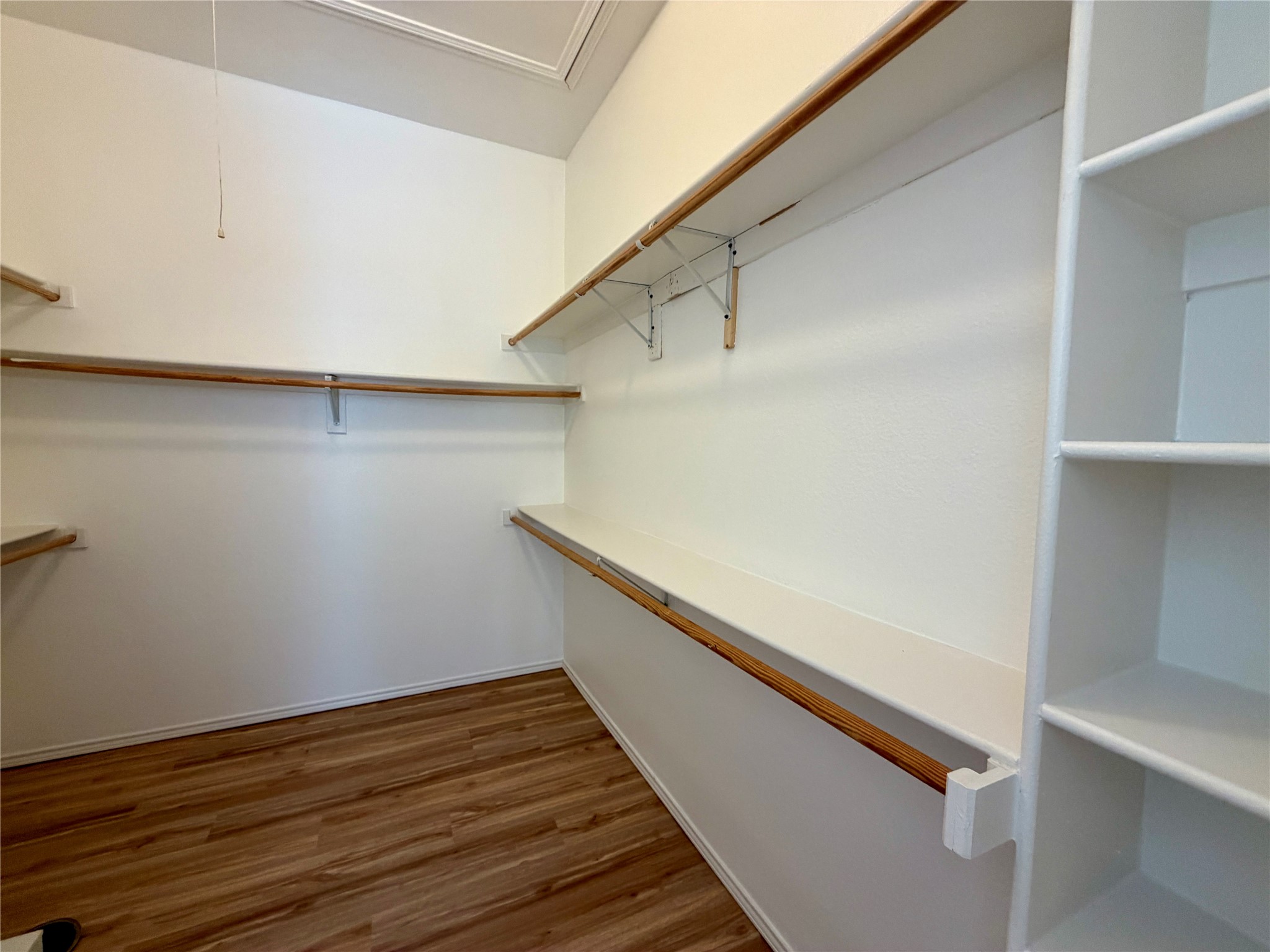Walk-in closet with wooden hanging rods, built-in shelves, and wood-look flooring.