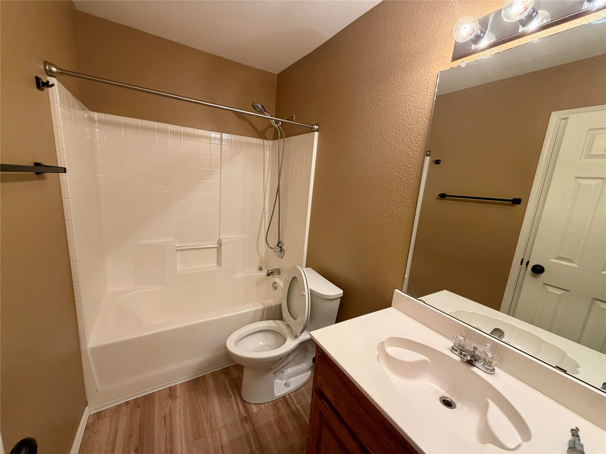 Bathroom with a white tub and shower, toilet, and wood-front vanity with a large mirror.