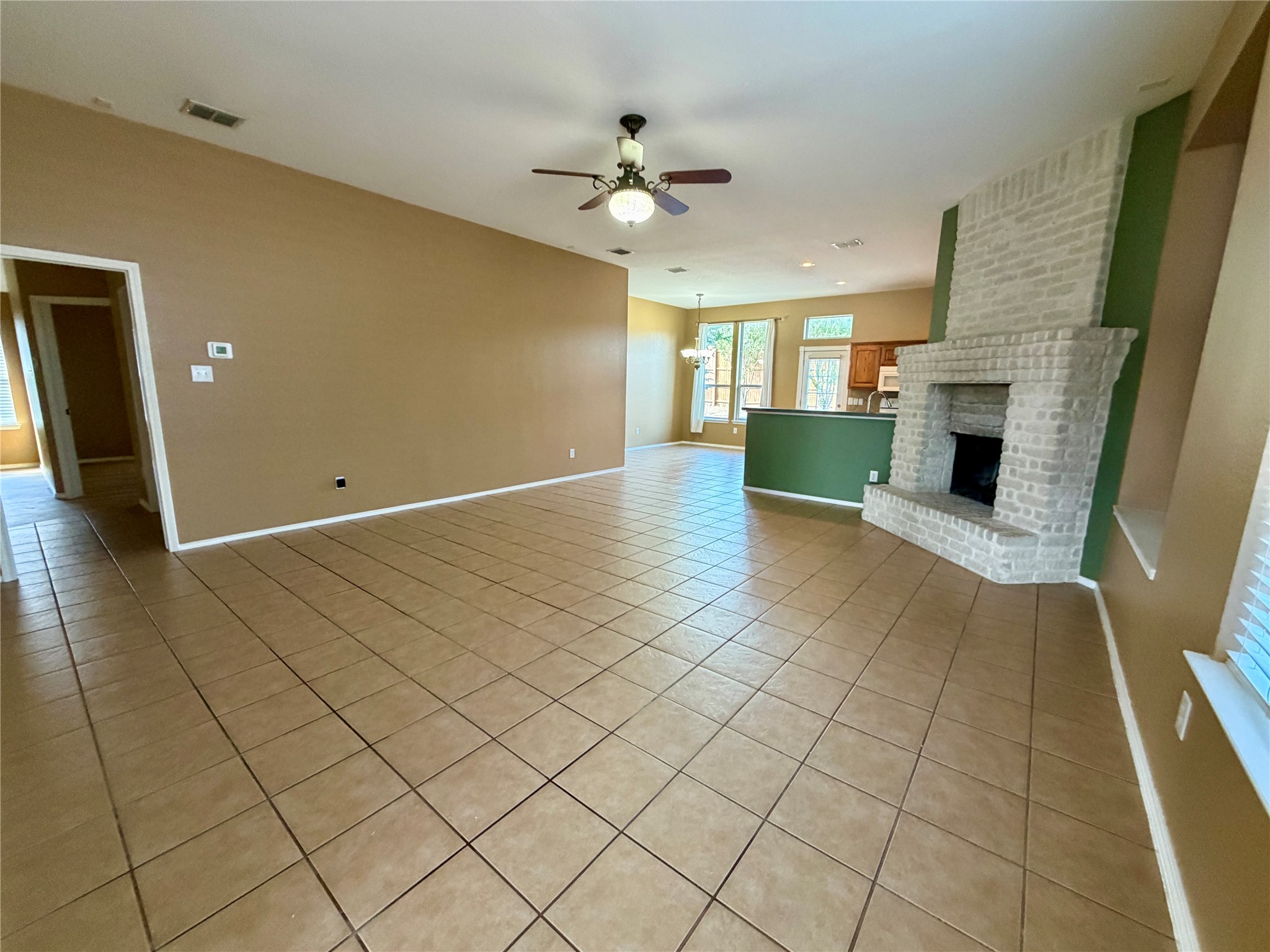 Vacant tiled living room with a white brick fireplace and green accent wall.