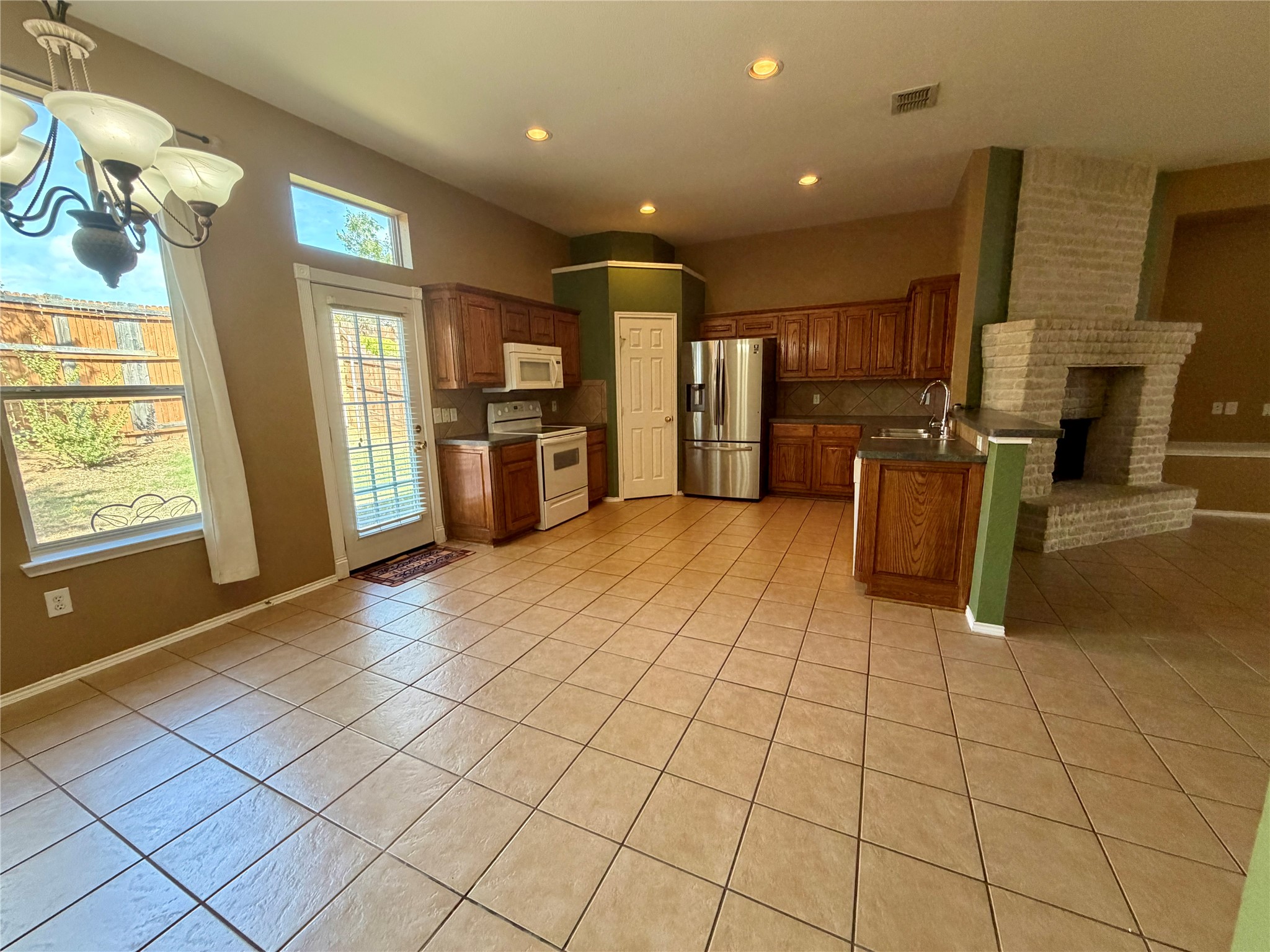 Kitchen with dark wood cabinets, stainless appliances, tiled floor, and a large light-brick fireplace.