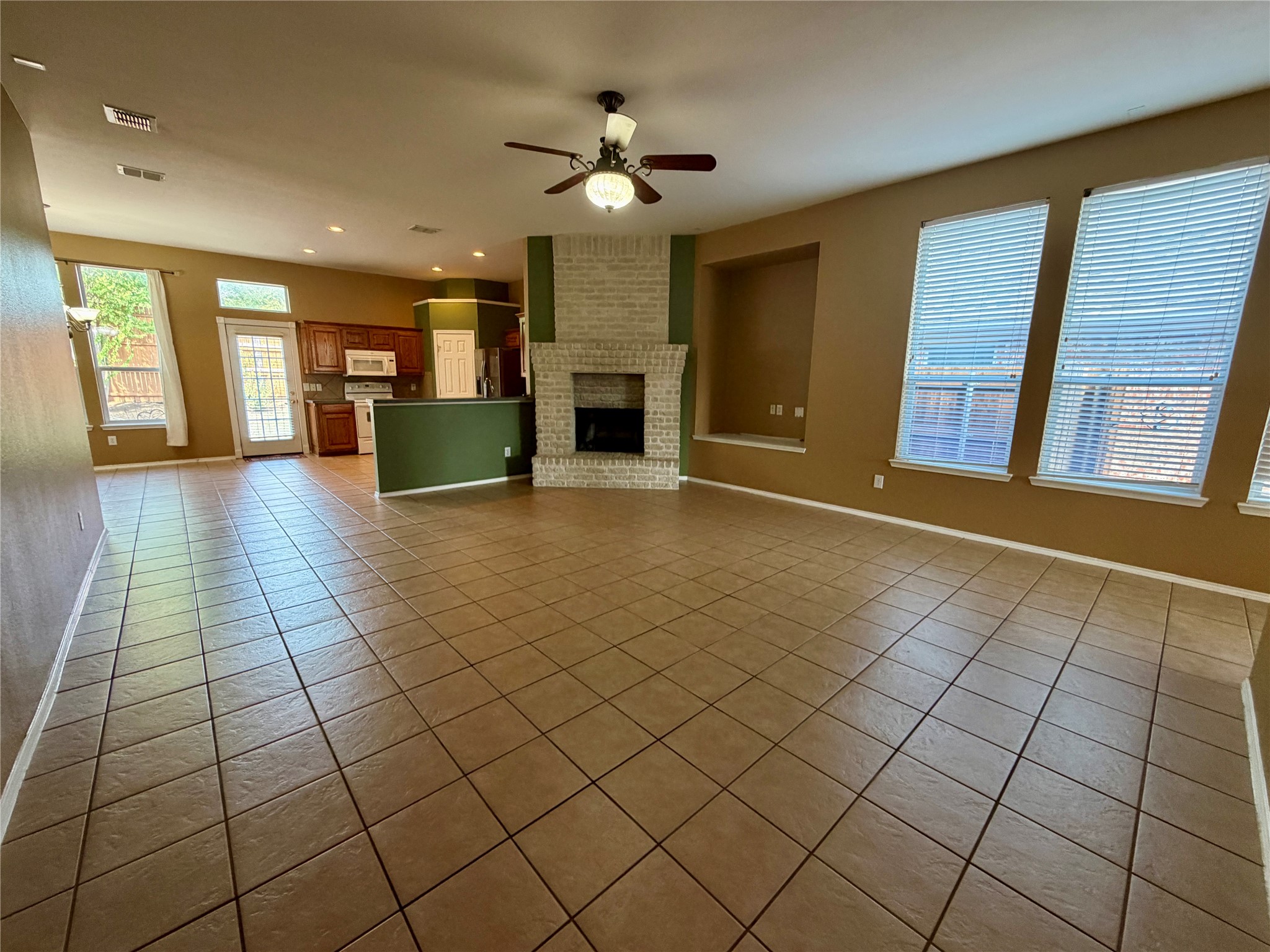 Empty living area with tile floors, a brick fireplace, and an adjoining kitchen.