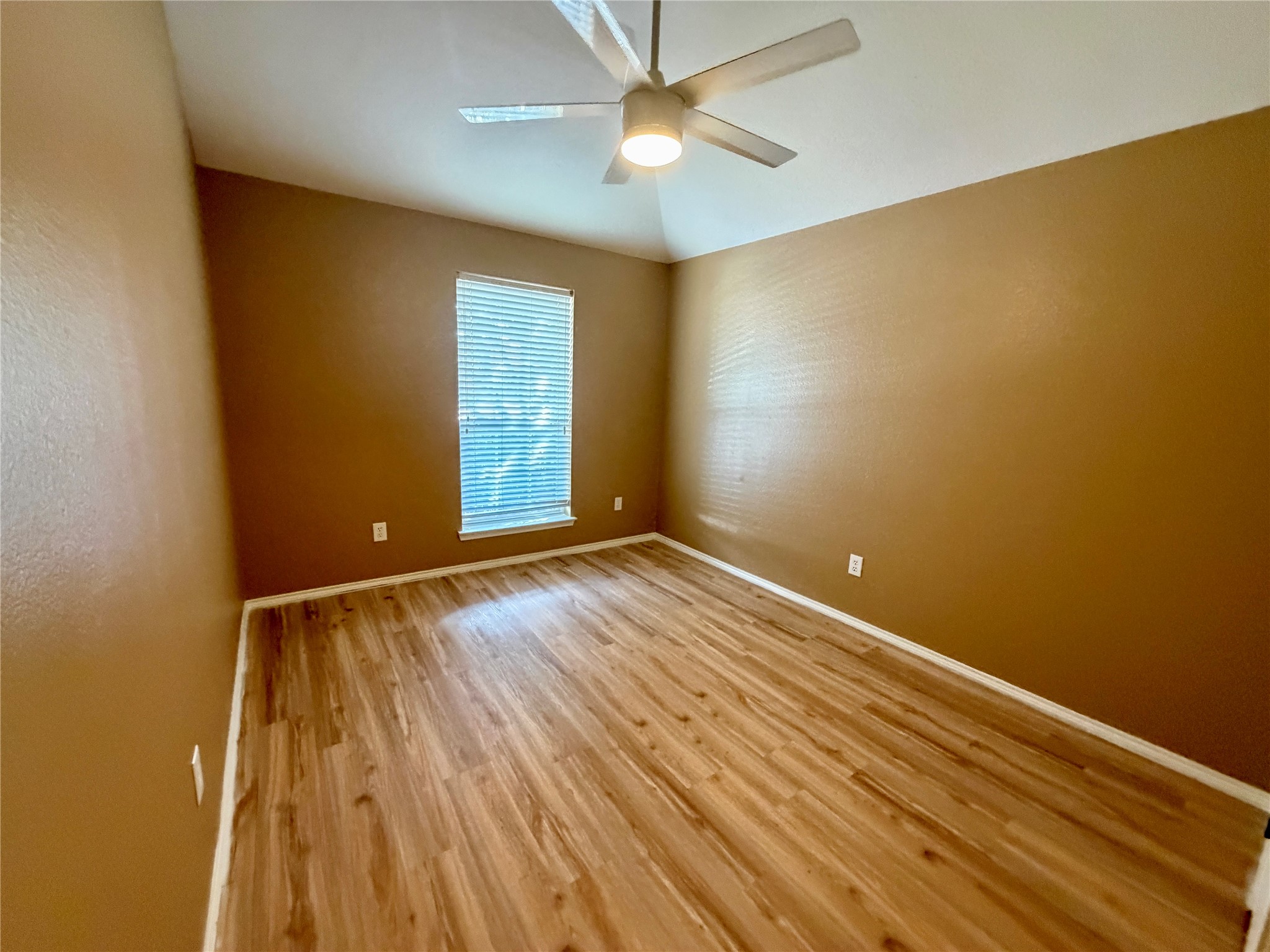 Empty room with wood-look flooring, brown walls, and a window with white blinds.