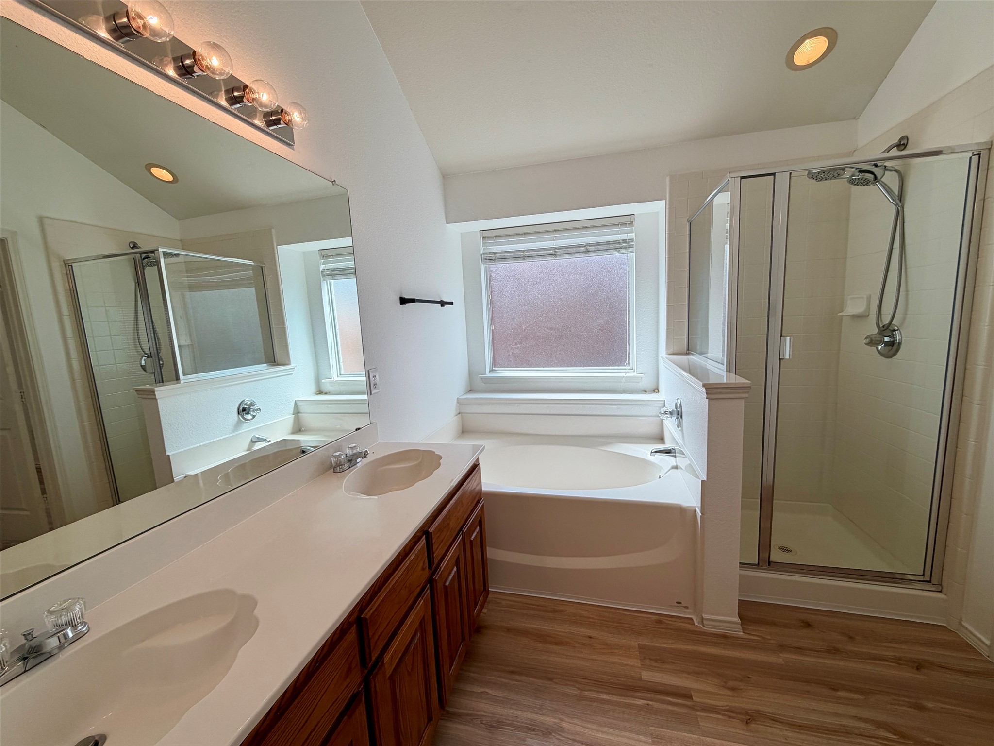 Bathroom with double-sink wood vanity, soaking tub beneath a window, and glass-enclosed shower.