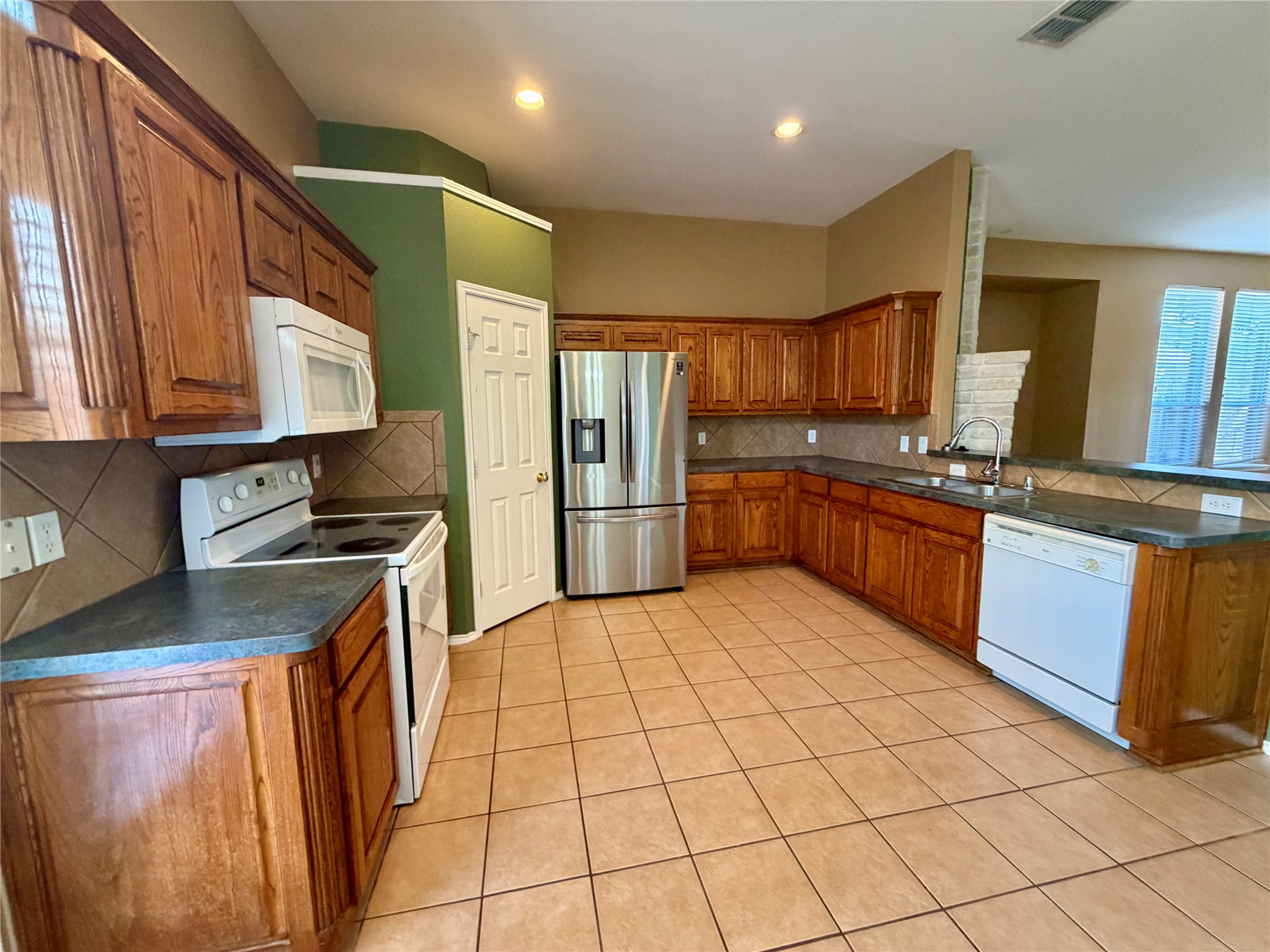 Kitchen with extensive wood cabinetry, tan tile floors, stainless steel refrigerator, and a pass-through counter.