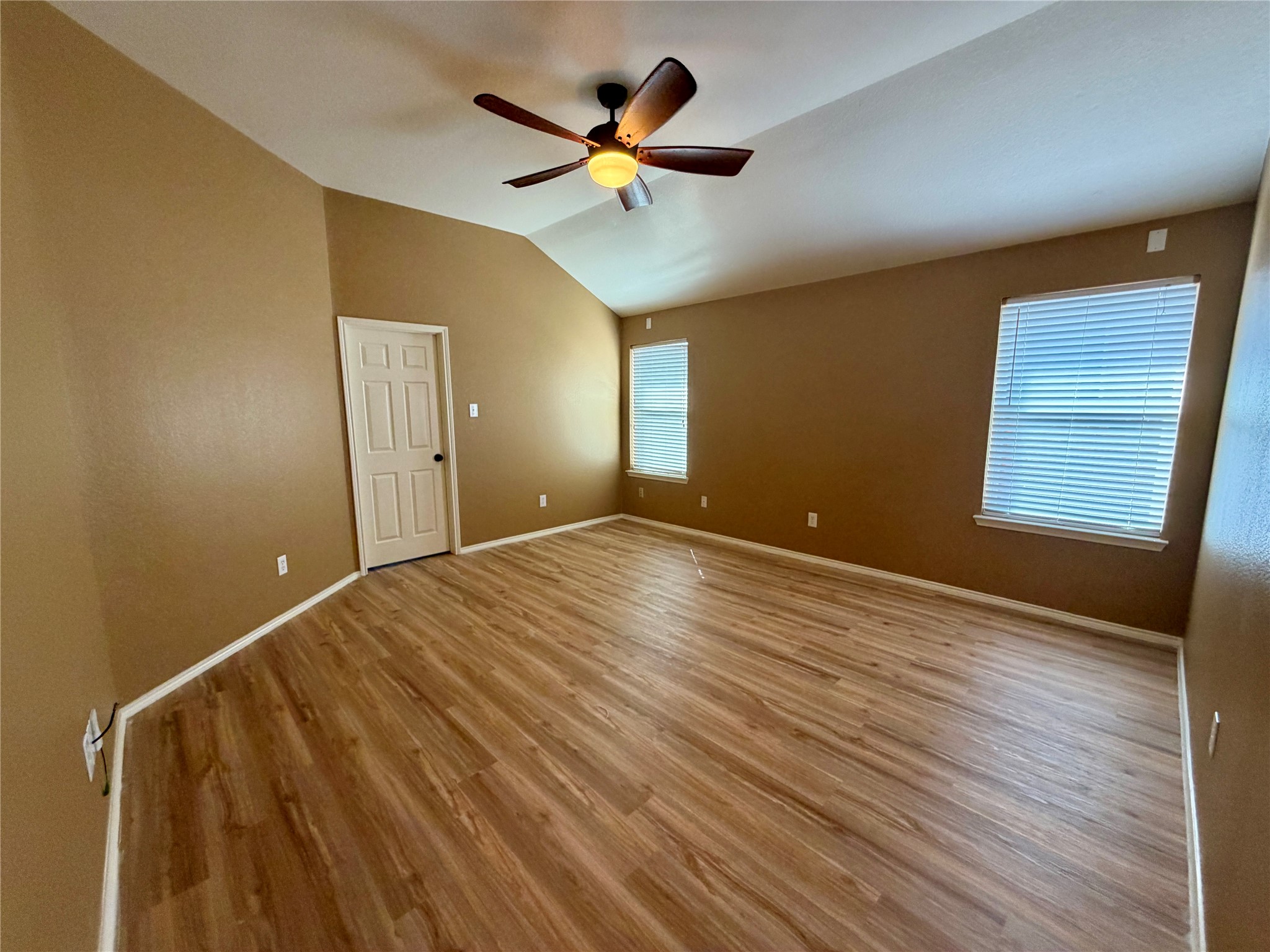 Empty room with wood-look floors, a vaulted ceiling, and two windows with blinds.