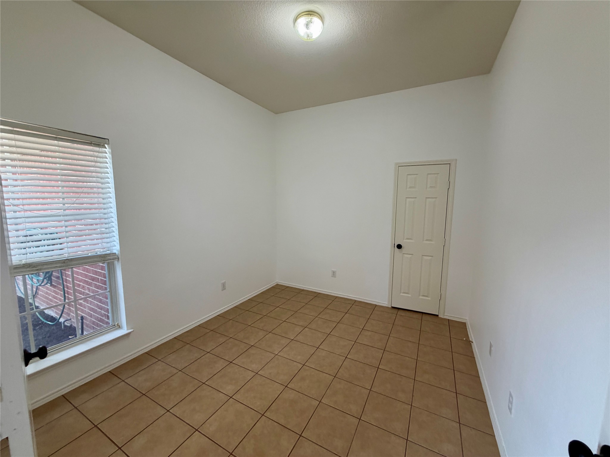 Empty room with tan tile flooring, white walls, and a window with blinds.