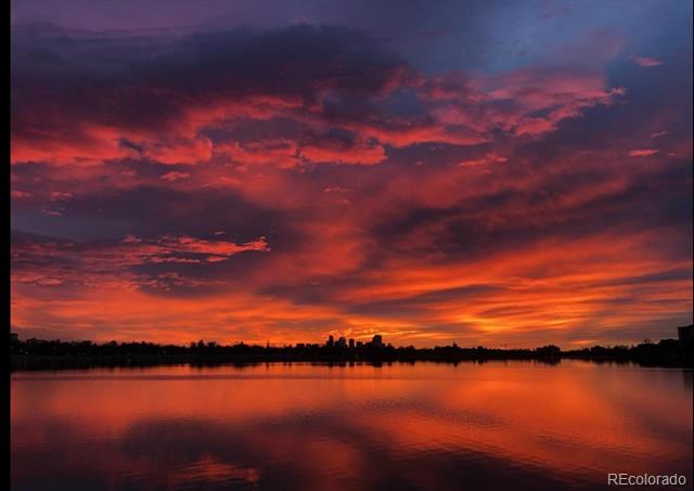 Sunset reflecting on a lake beneath a distant city skyline.