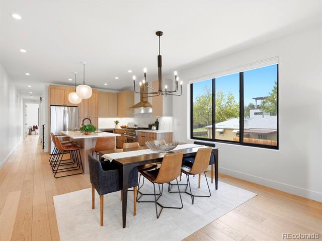 Open-plan dining room and kitchen with a large table, light wood floors, and wide windows.