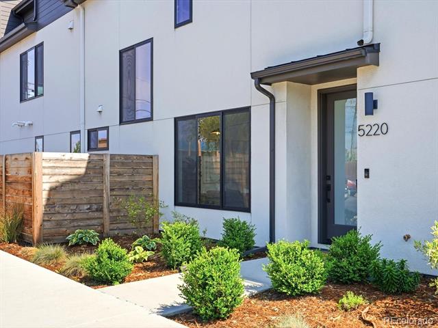 Modern white home entrance with dark-framed windows, landscaped shrubs, and the number 5220.
