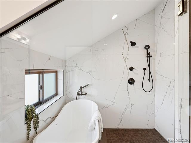 Bathroom with a freestanding soaking tub, marble-look tile, and black shower fixtures.