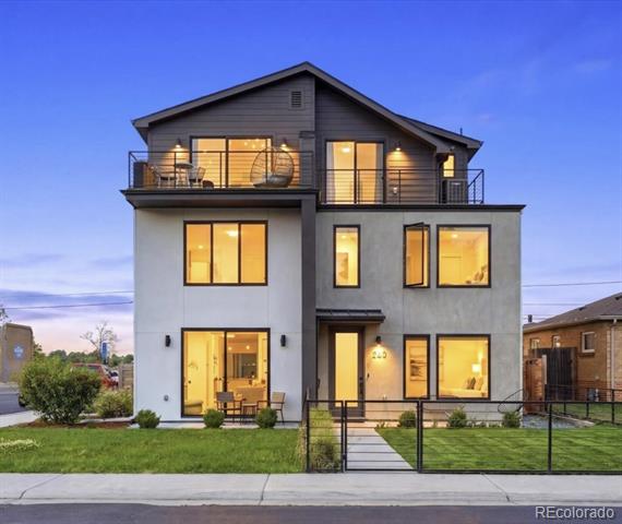 Modern two-story home with an upper balcony and illuminated windows at dusk.