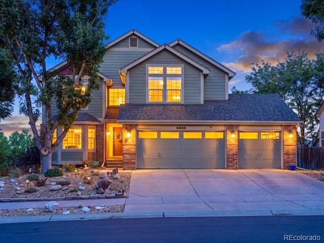 Two-story gray house at dusk with illuminated windows, stone accents, and a three-car garage.