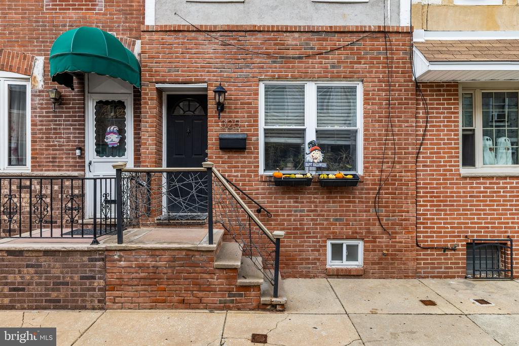 Brick rowhouse exterior with a green awning, raised stoop, and Halloween decorations in the windows.