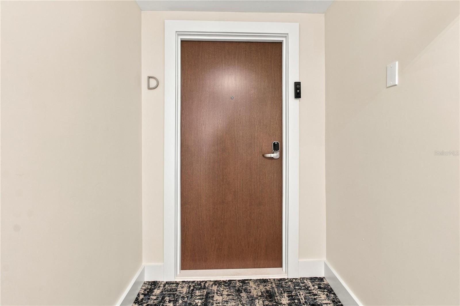 Condo entry hallway with a brown door, electronic lock, D marker, and patterned carpet.