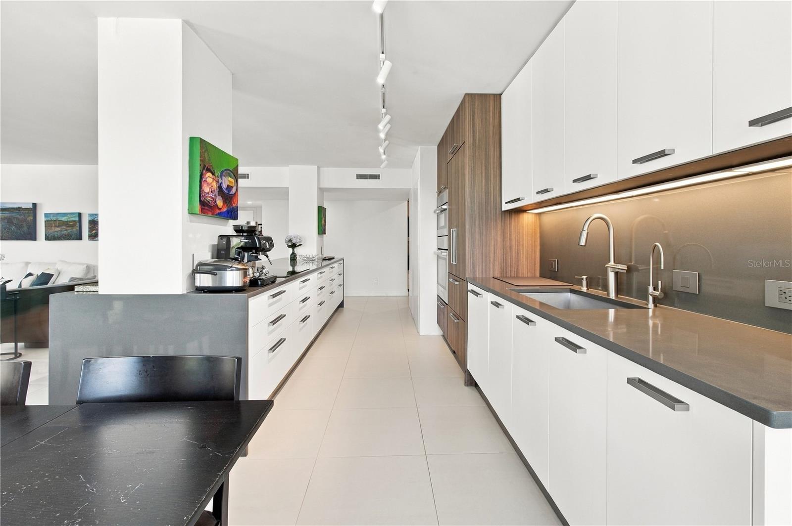 Modern kitchen with white cabinets, dark counters, stainless steel appliances, and a long central island.