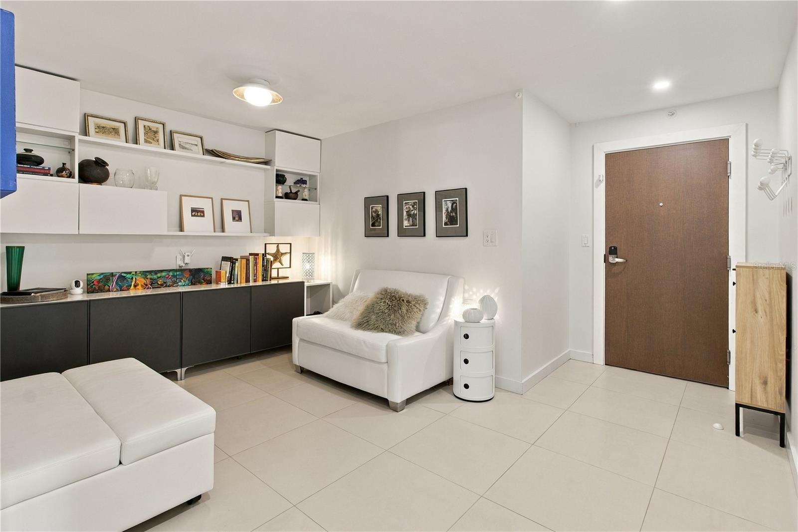 Furnished condo entry with white seating, built-in shelving, and a brown front door.