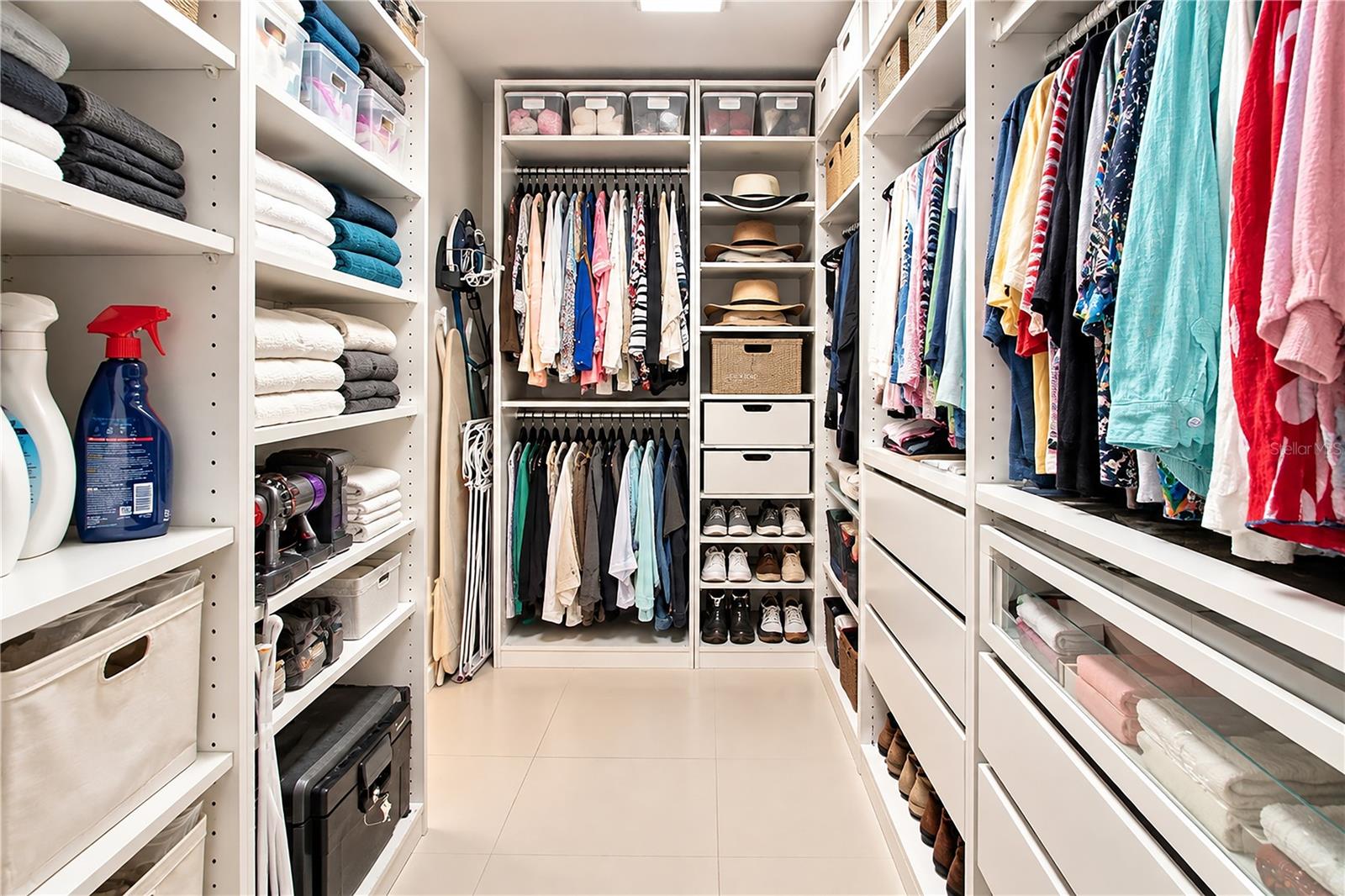 Walk-in closet with extensive built-in storage, hanging clothes, folded towels, and neatly arranged shoes.