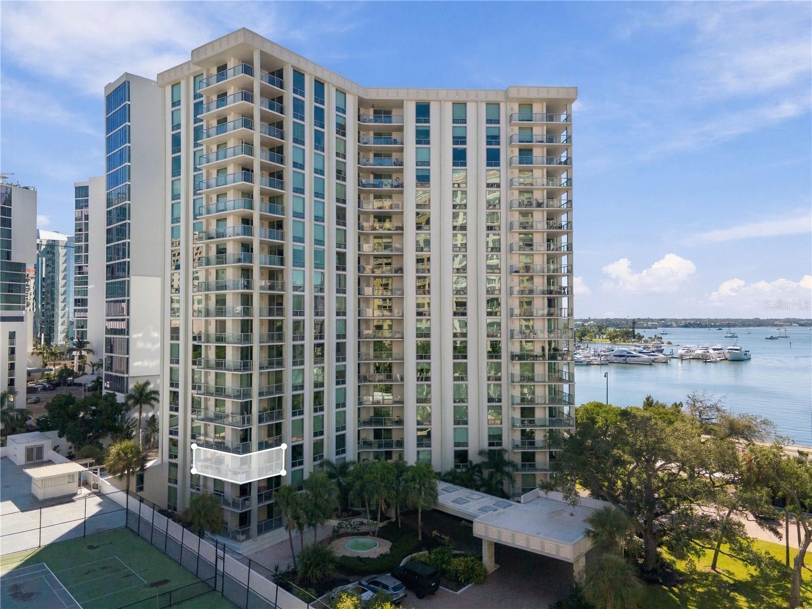 White condominium tower with glass balconies overlooking a marina; one balcony is outlined.