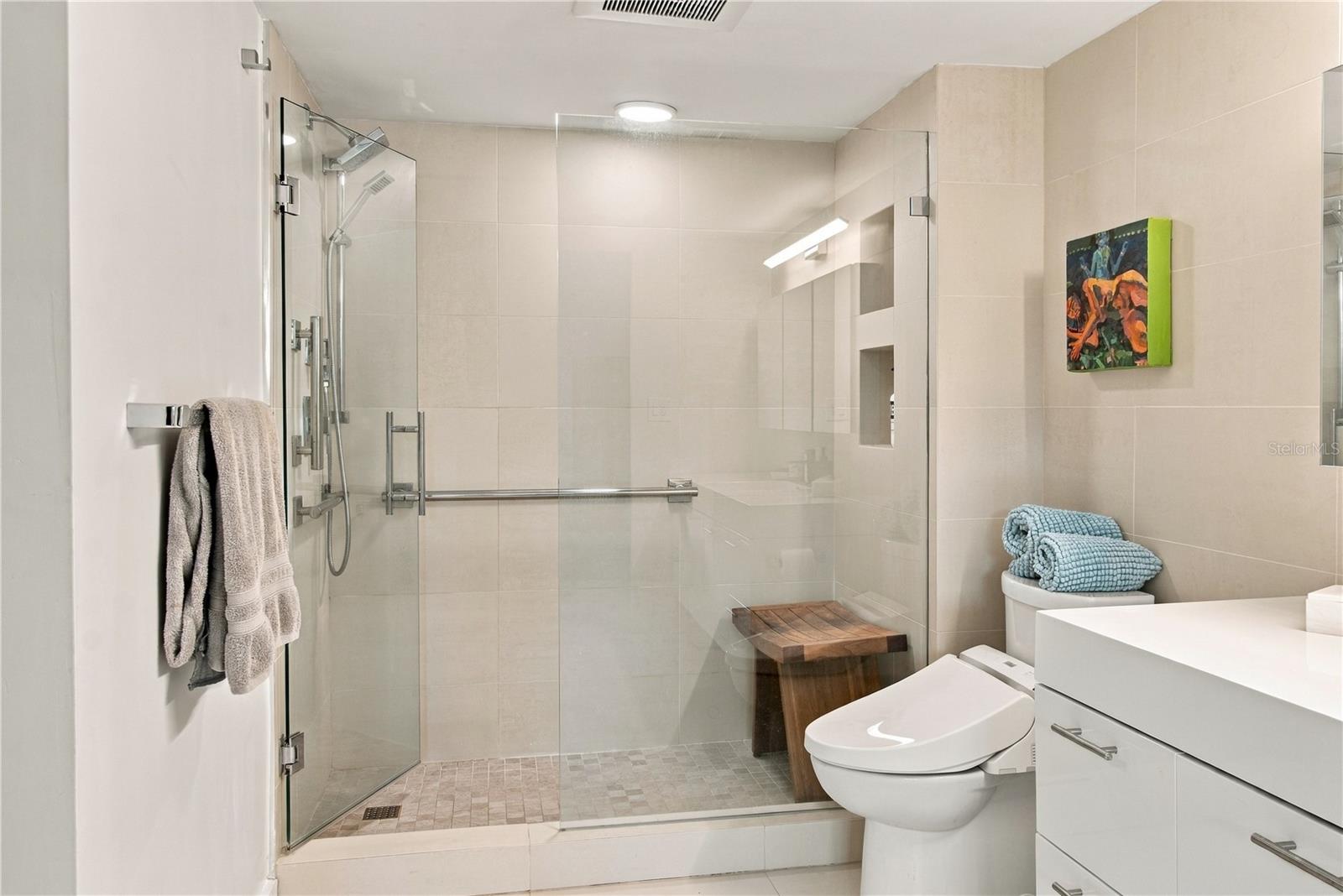 Bathroom with a spacious glass-enclosed shower, beige tile, and white vanity.