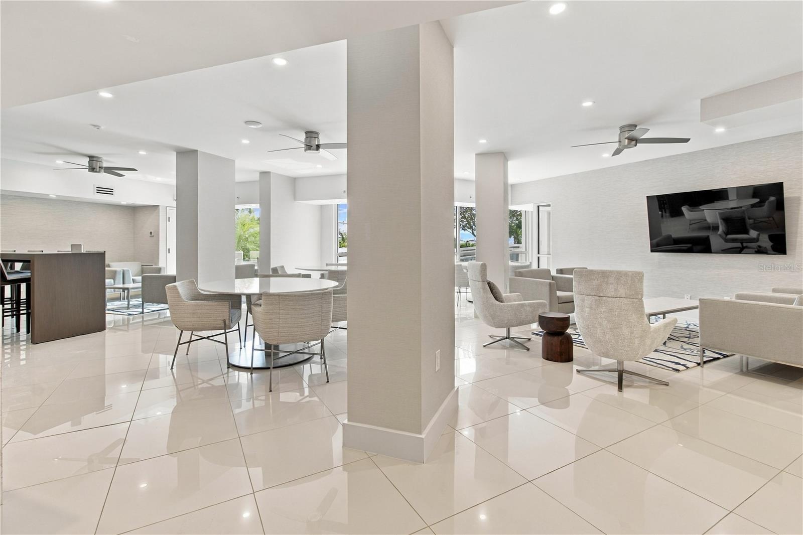 Furnished condo lounge with dining and seating areas, glossy tile floors, and large windows.
