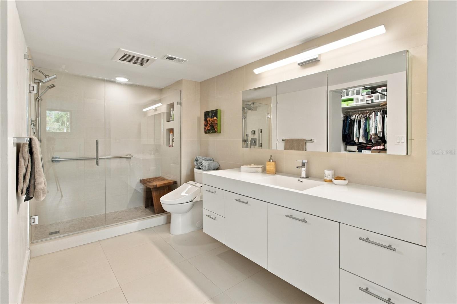 Modern bathroom with a long white vanity, mirrored cabinets, and glass-enclosed shower.