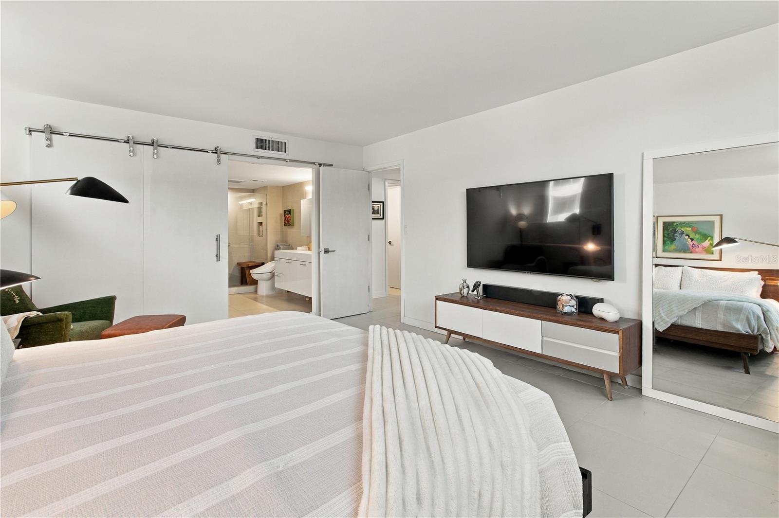 Furnished bedroom with a large bed, wall-mounted television, and open ensuite bathroom.