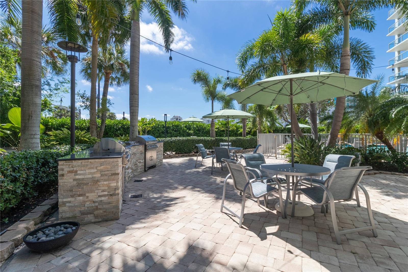 Condominium patio with umbrella-shaded seating, built-in grills, and palm trees.