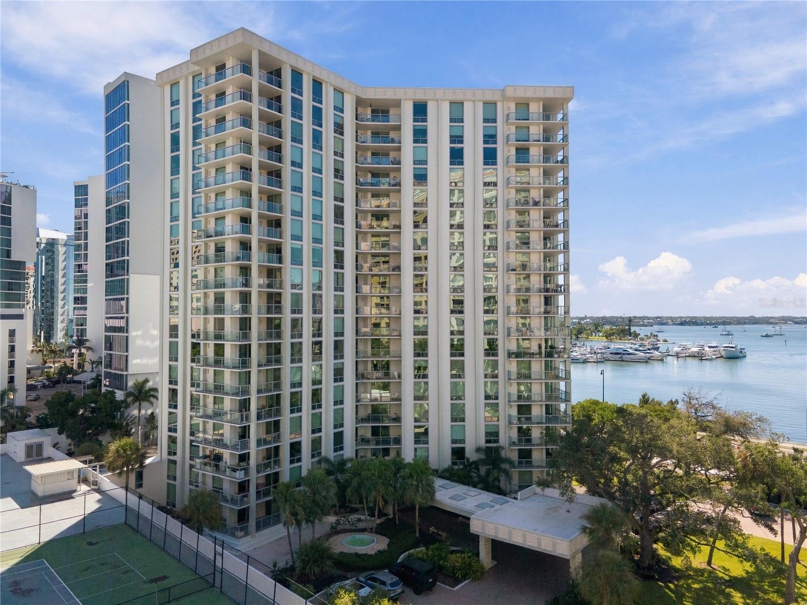 High-rise condominium with glass balconies overlooking a marina and boats.