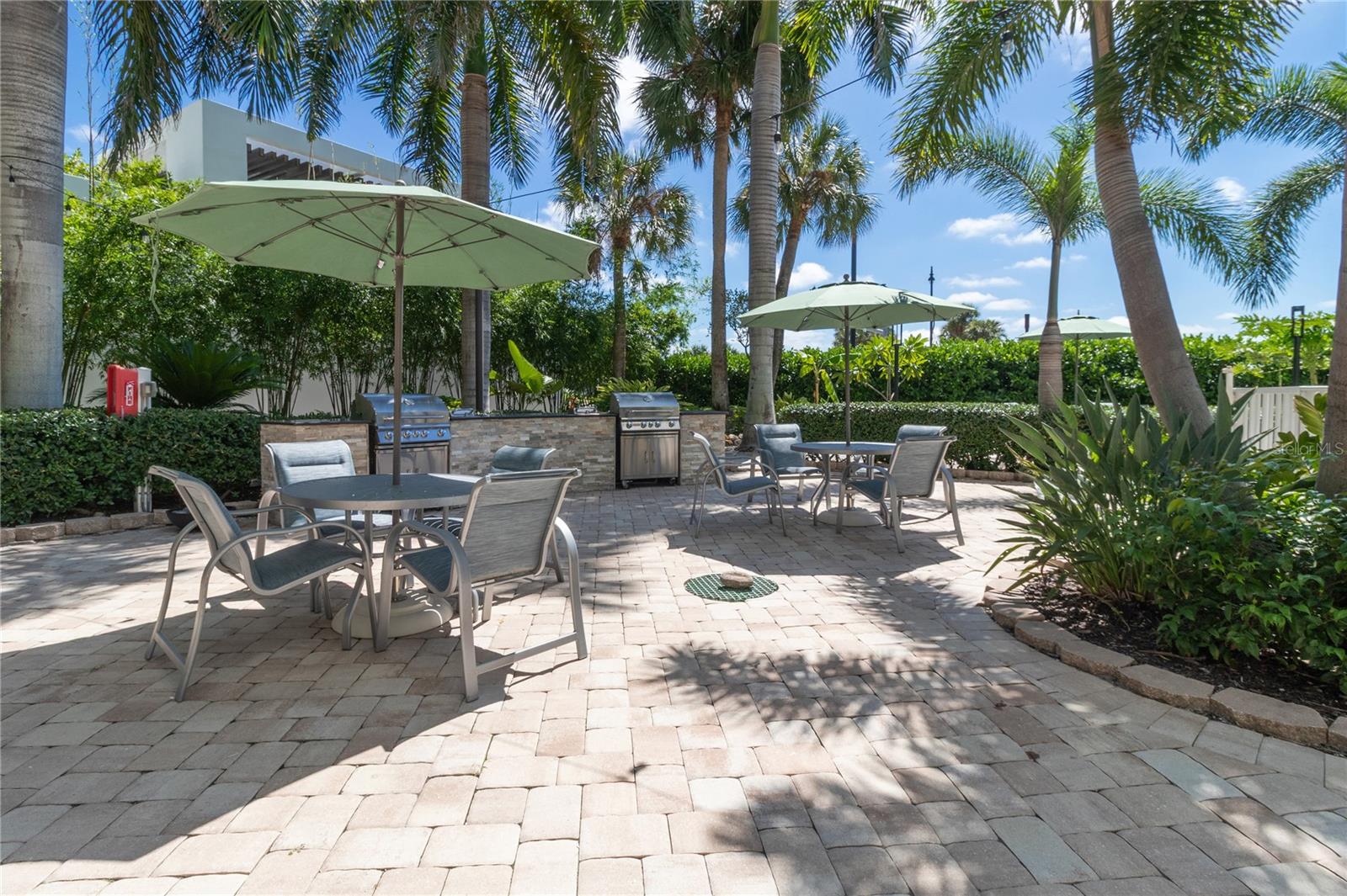 Outdoor patio with shaded dining tables, palm trees, and a built-in grilling area.