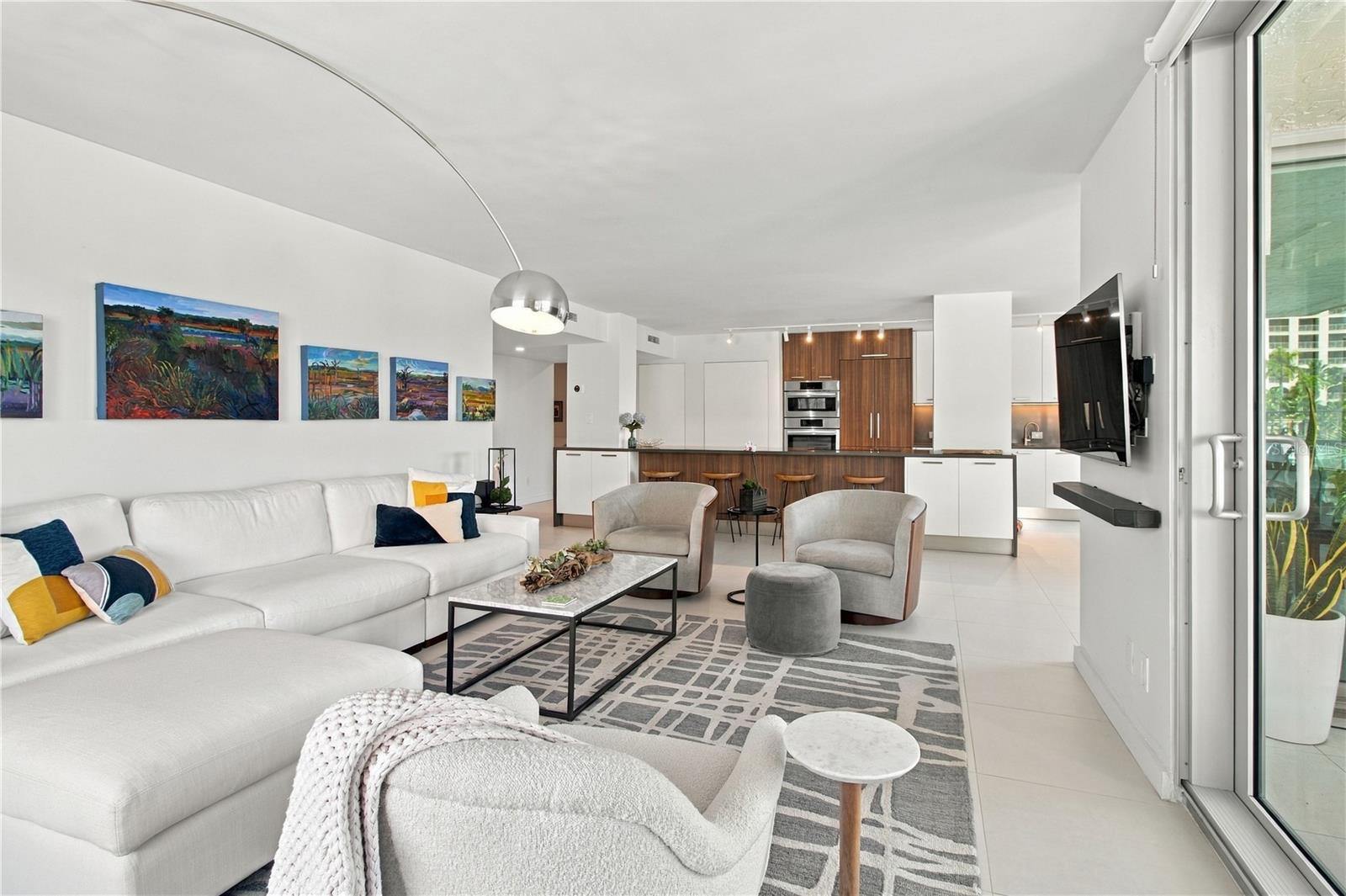 Open-plan condo living room with a white sectional, colorful artwork, and a modern wood-accented kitchen.