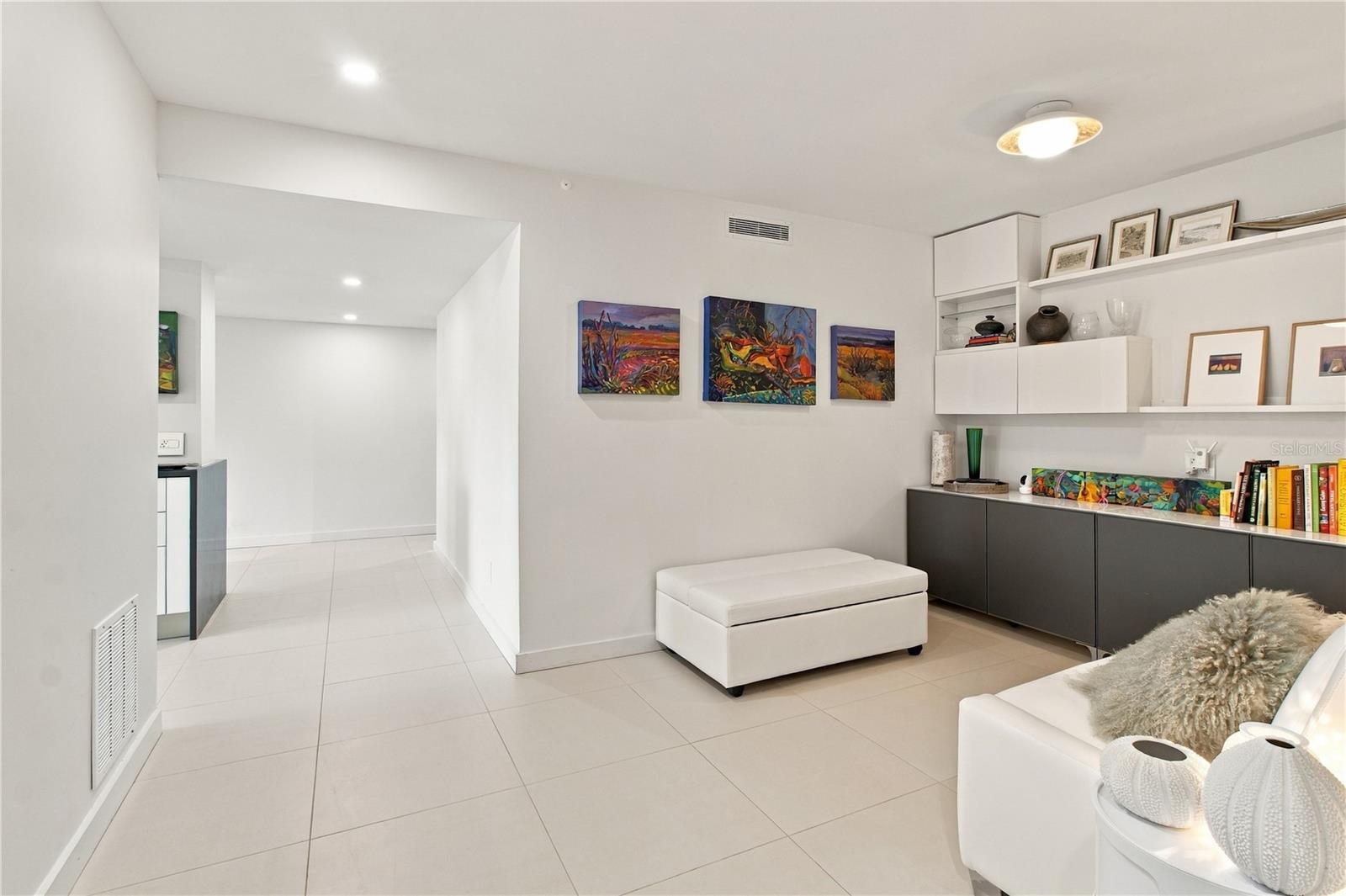 Furnished condo living area with colorful wall art, white seating, and built-in shelving.