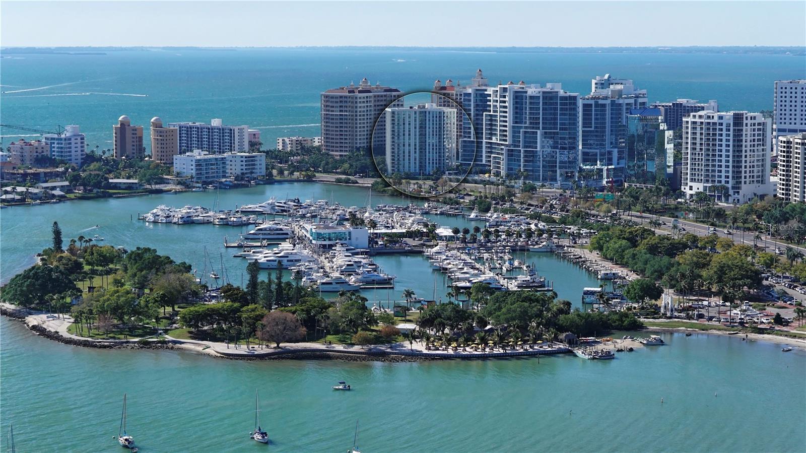 Aerial waterfront view of Sarasota high-rises, with a circle highlighting one building beside a marina.