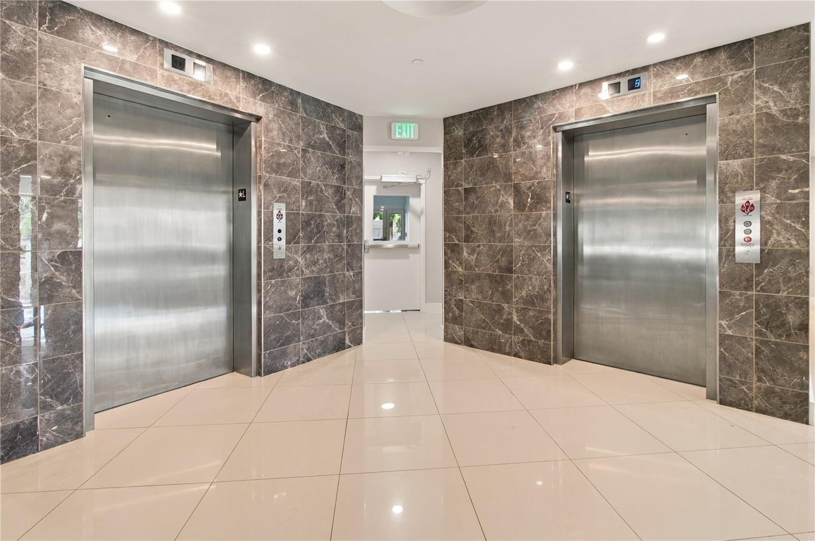 Condominium elevator lobby with two stainless steel elevators and dark marble-patterned walls.