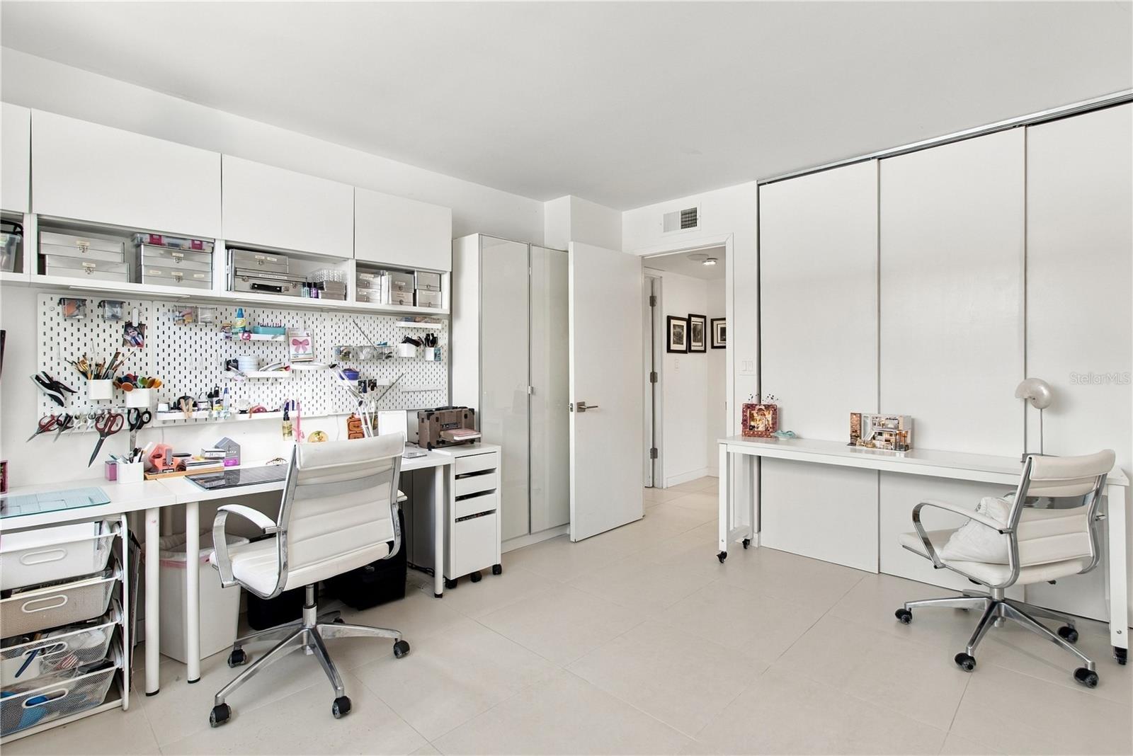 Office with built-in cabinets, a pegboard craft workspace, and two white desks and chairs.