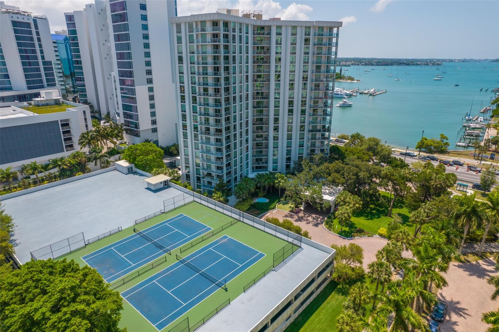 Waterfront condominium tower overlooking tennis courts and Sarasota Bay, with boats in the marina.