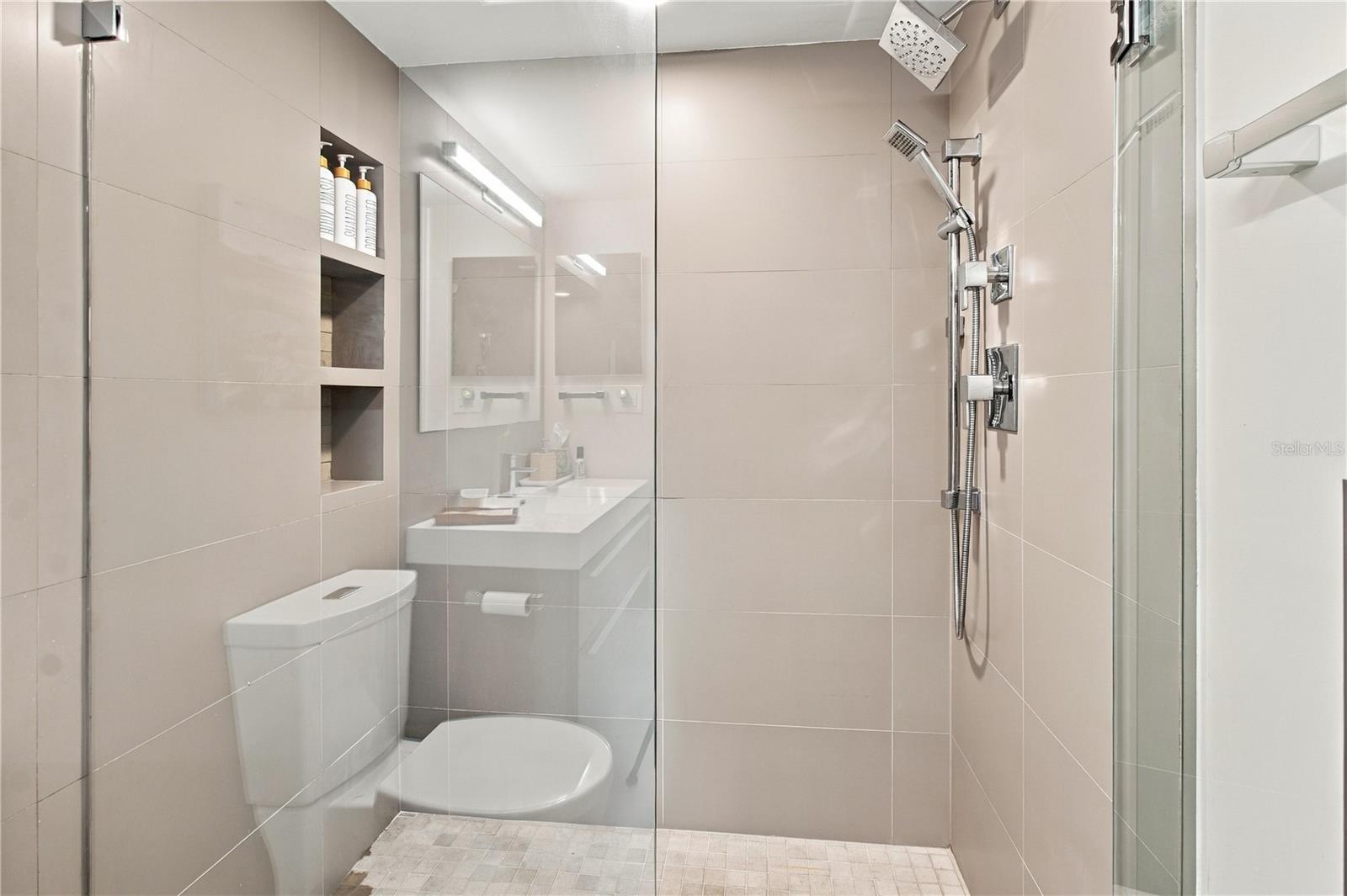 Modern tiled bathroom with a glass shower, rain showerhead, recessed niches, and floating vanity.