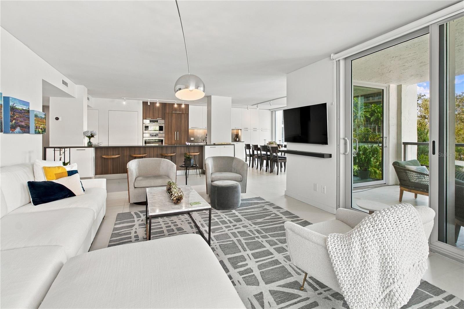 Open-plan living room with white seating, dark wood kitchen cabinetry, and sliding doors to a balcony.