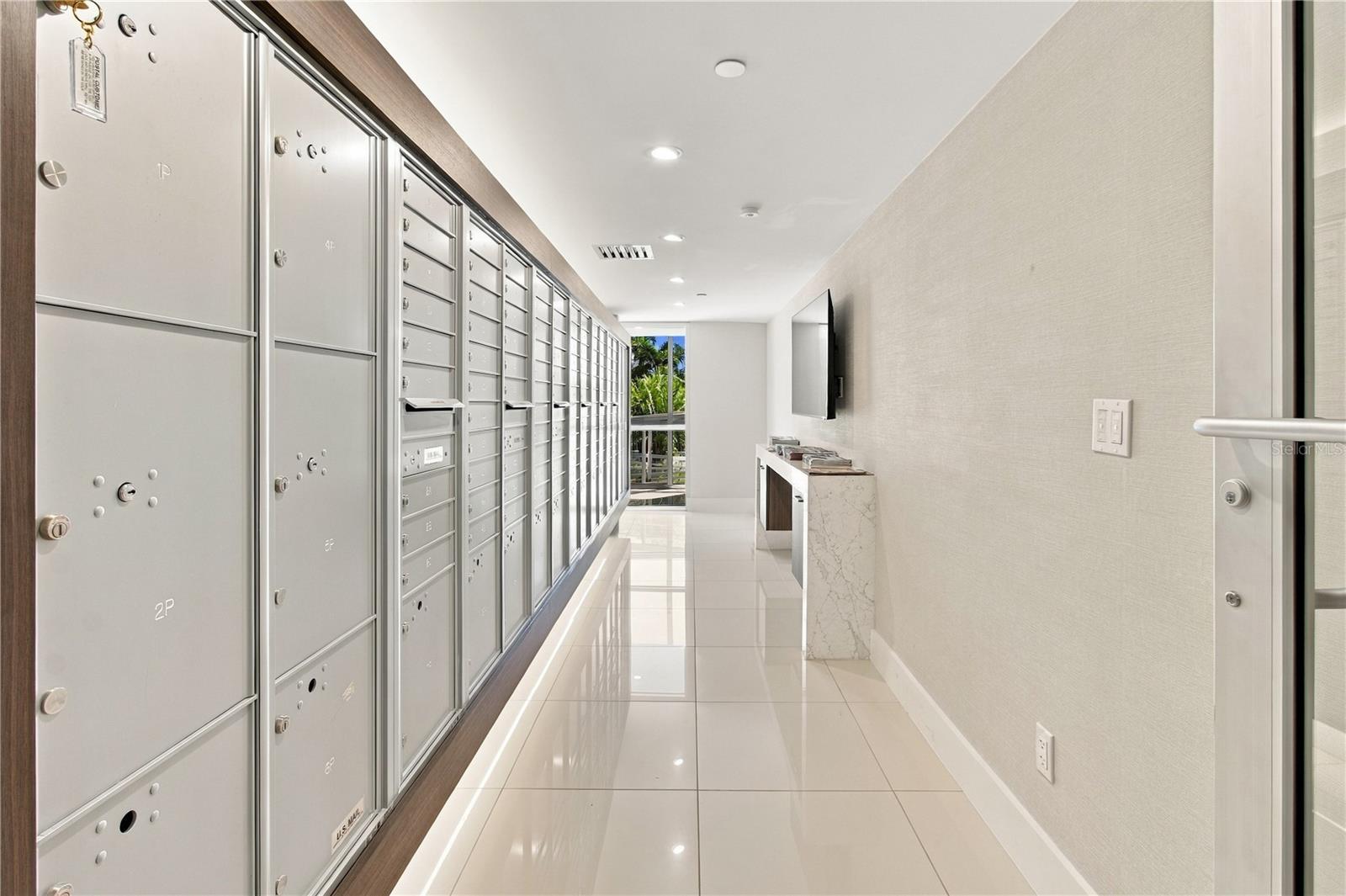 Condominium mailroom corridor with silver mailboxes, glossy tile floors, and a marble-front counter.